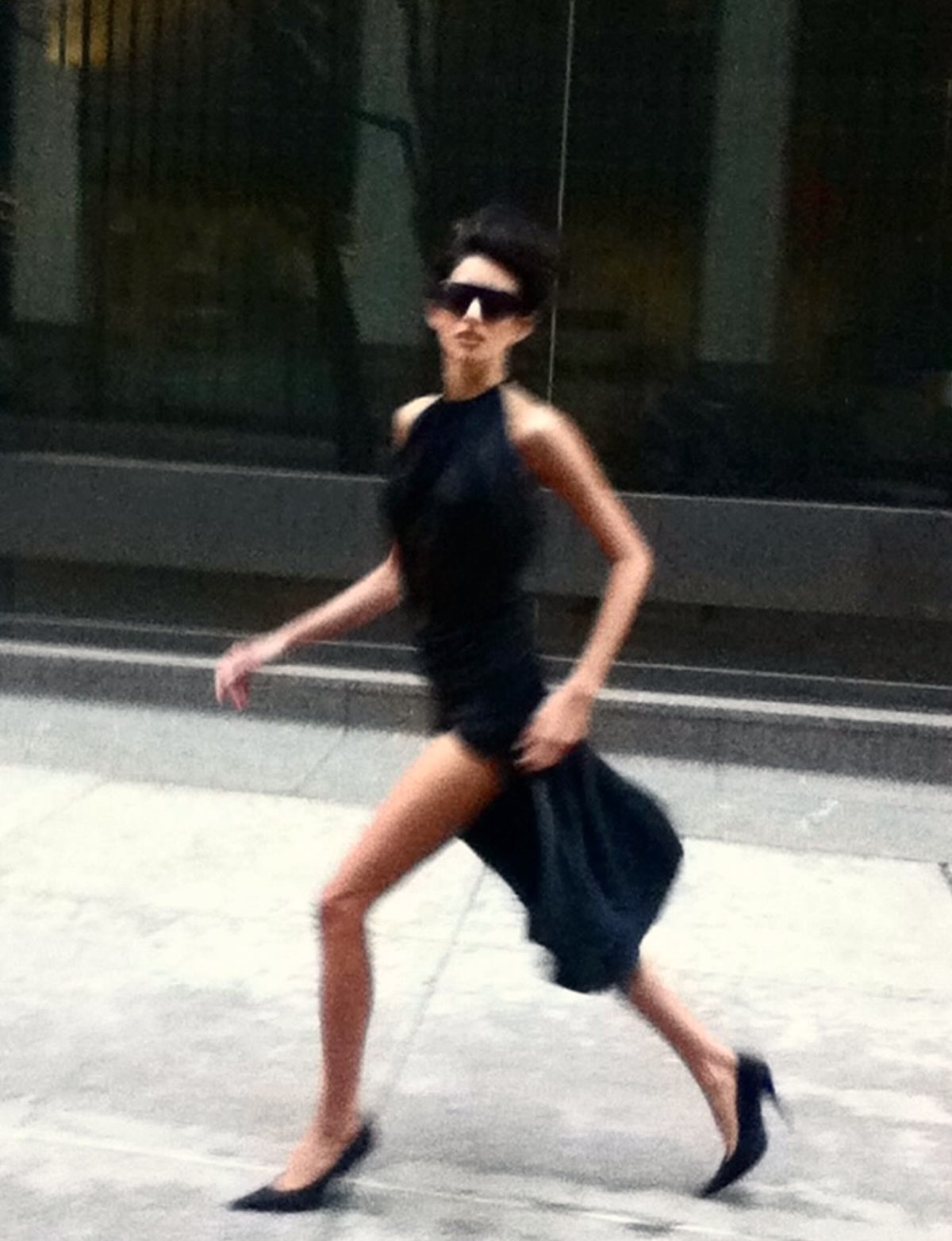 Woman in black dress and sunglasses walking with motion blur