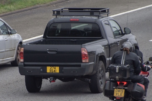 Plaque 274 X 641 — États-Unis, personnel non diplomatique, Londres Plaque diplomatique britannique jaune 274 X 641 sur un Toyota Tacoma noir sur autoroute à Londres — code 274 États-Unis, statut X (personnel non diplomatique)