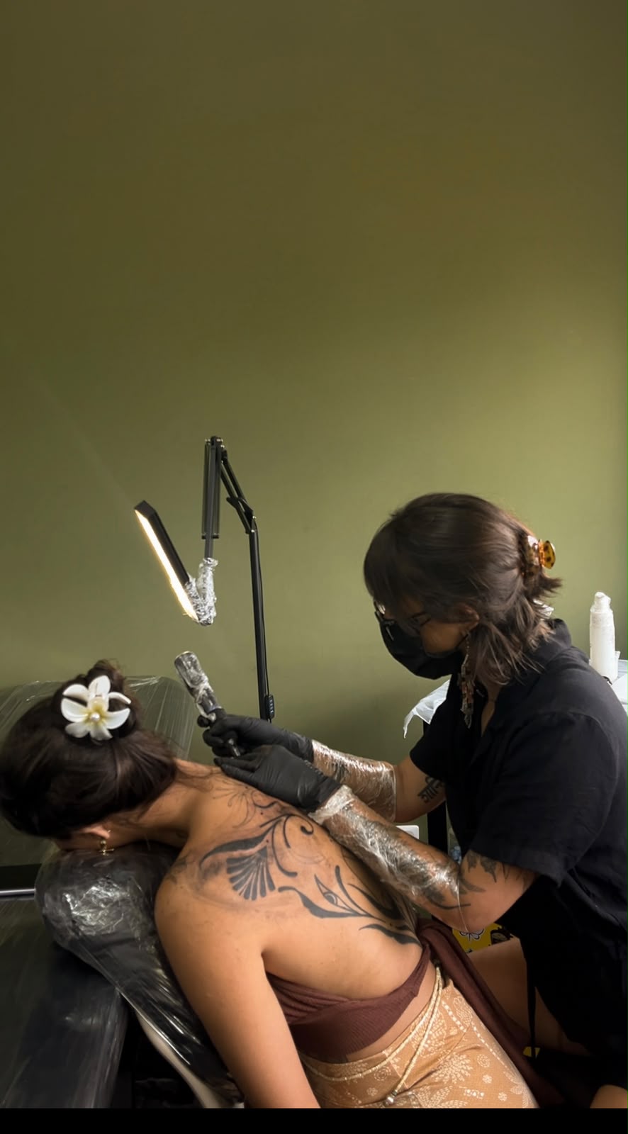 Cecília tatuando uma cliente, fundo verde