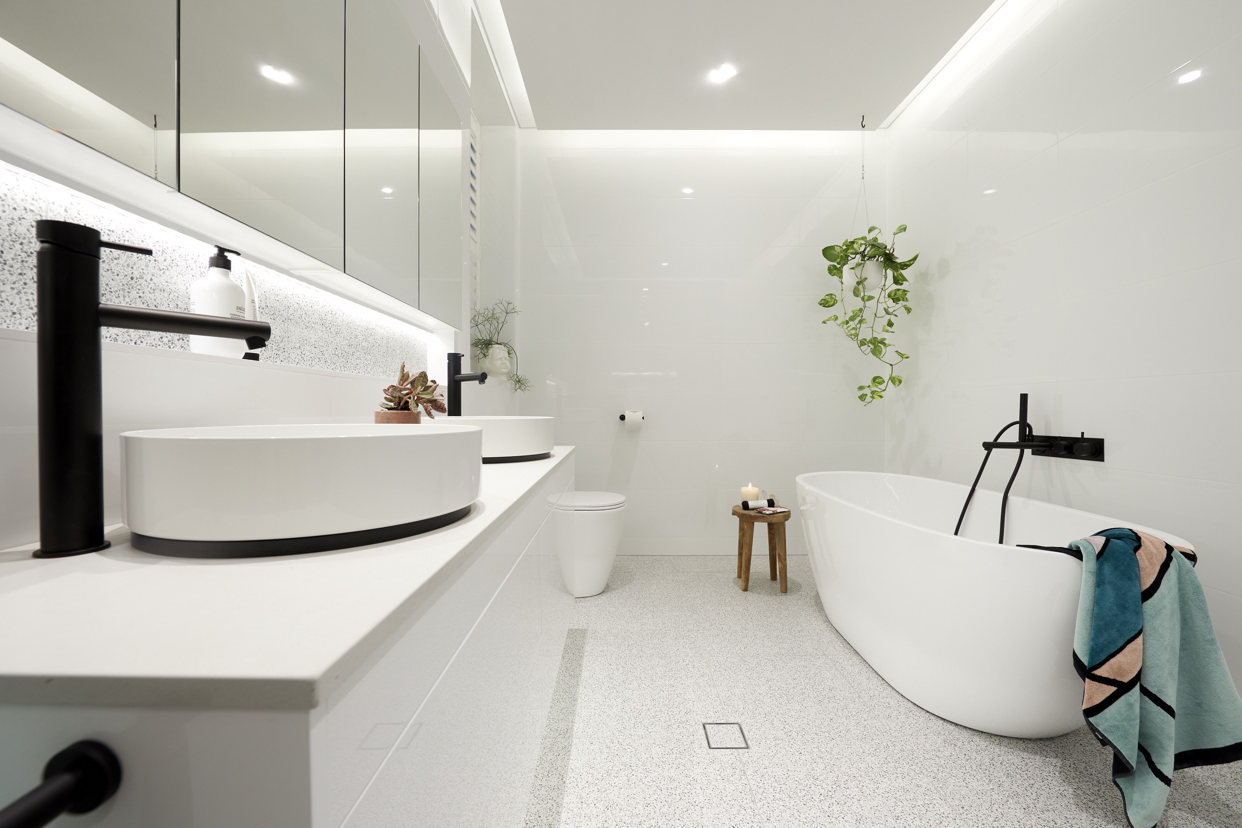 Modern minimalist bathroom with white vanity, black fixtures, freestanding soaking tub, and terrazzo flooring