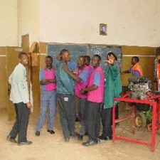 Schüler in pinken und blauen Overalls bei technischer Schulung vor der Tafel