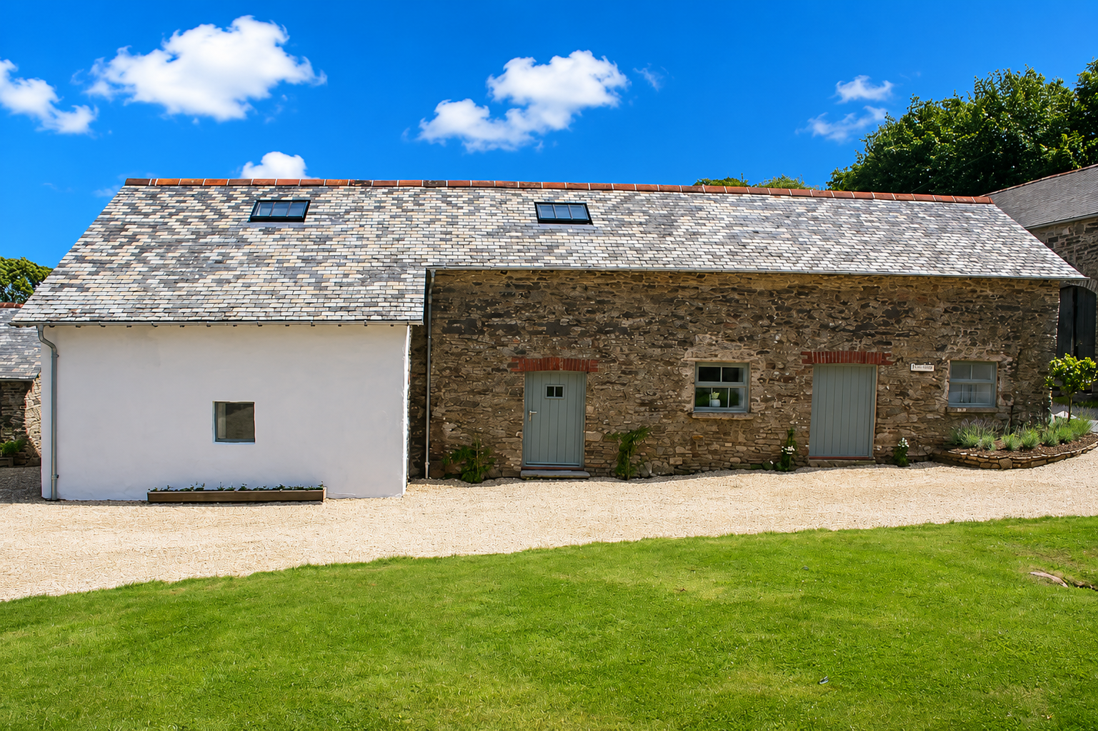 Stone barn exterior with slate roof, sage-green doors, and gravel driveway