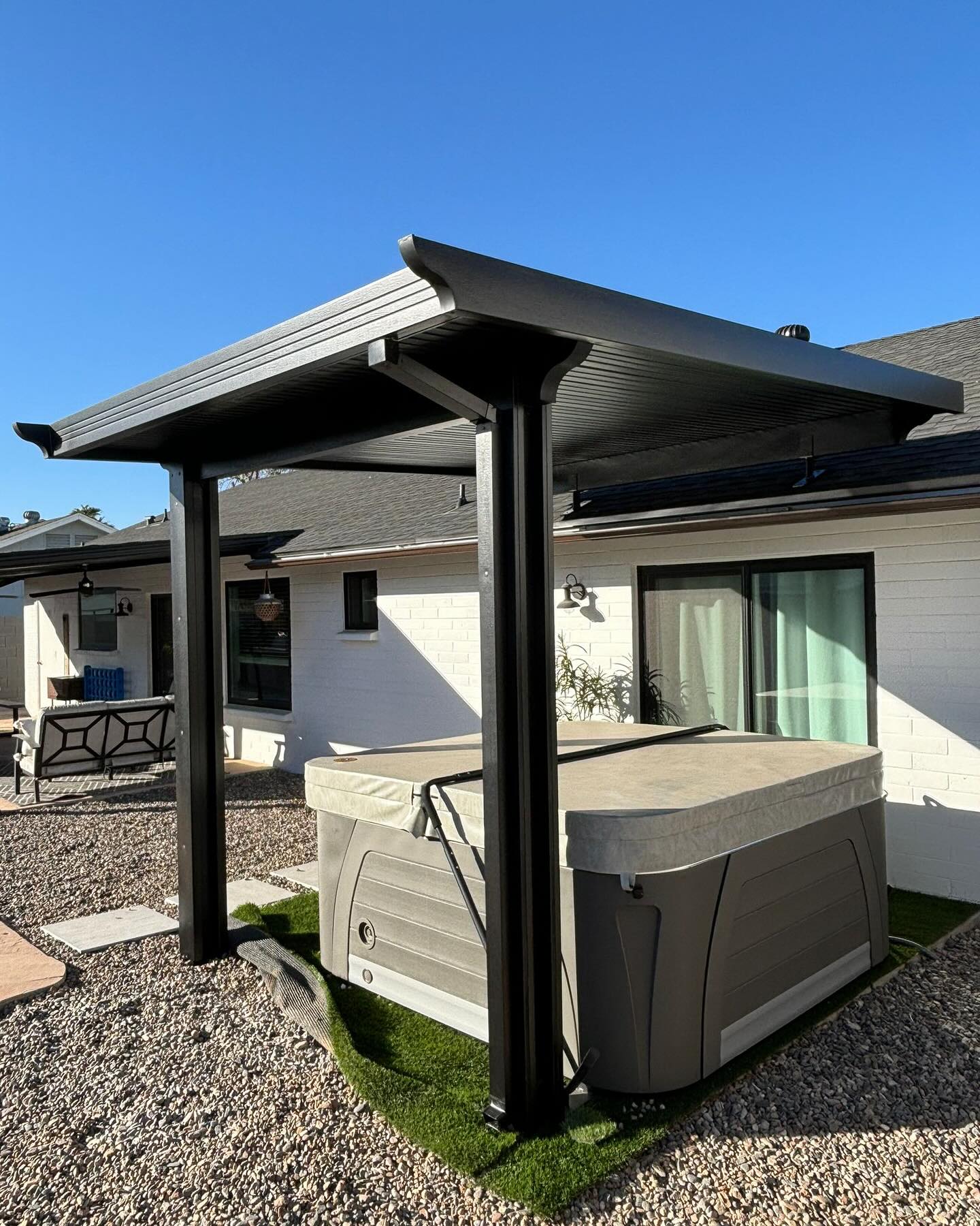 Freestanding patio cover shading a hot tub on artificial turf