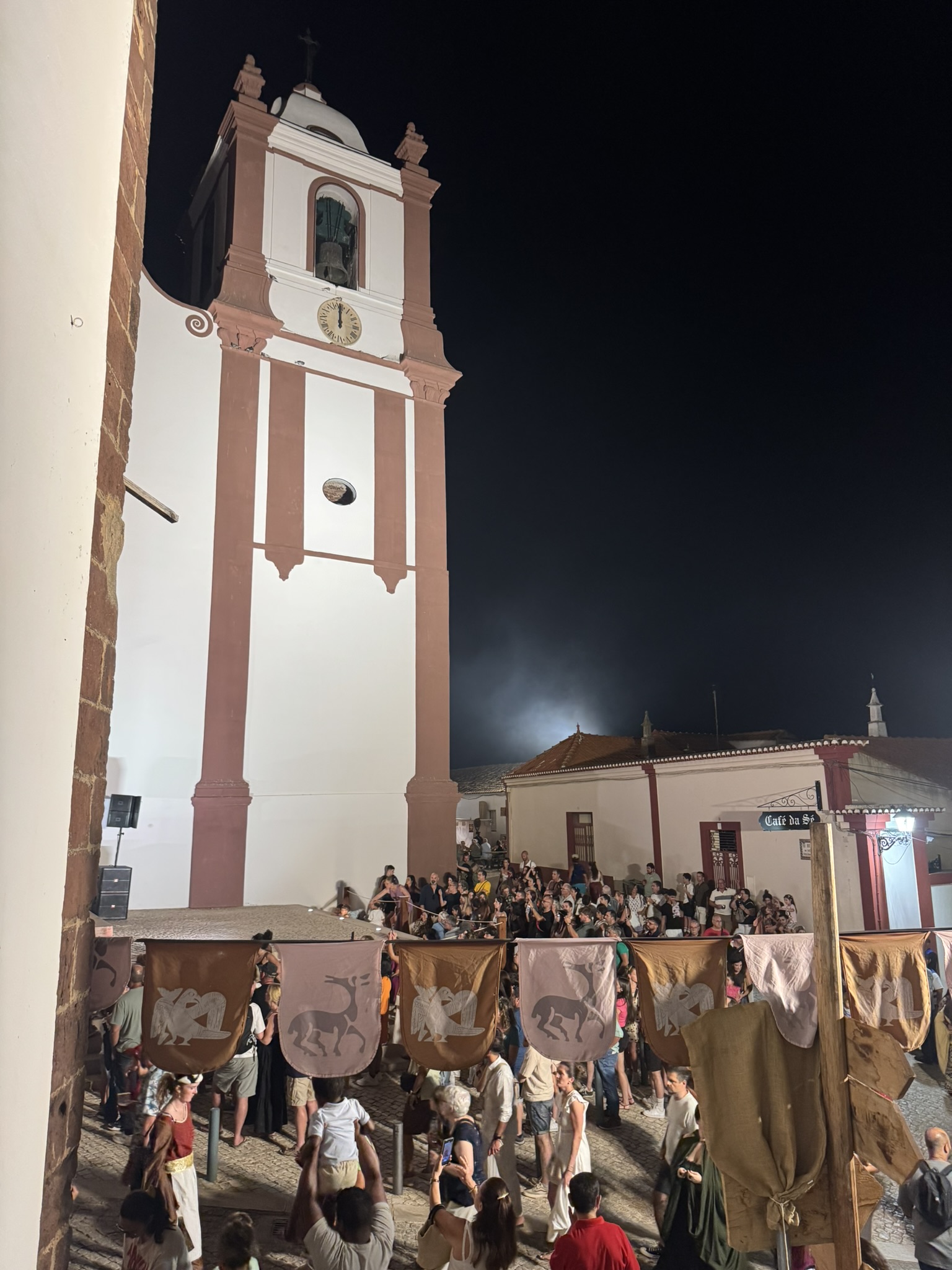 Crowds and heraldic banners beneath the church tower at the Silves Medieval Fair at night