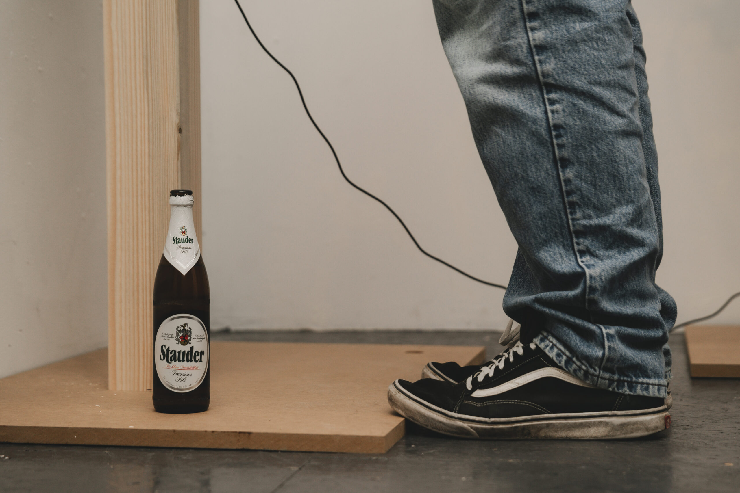 Stauder-Bierflasche neben einem Holzpodest mit Audiokabel – Ausstellungsaufbau