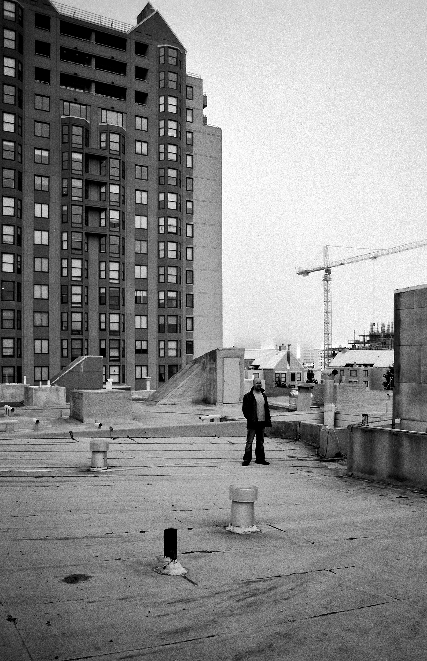 Man standing on urban rooftop with high-rise building and construction crane in San Francisco skyline