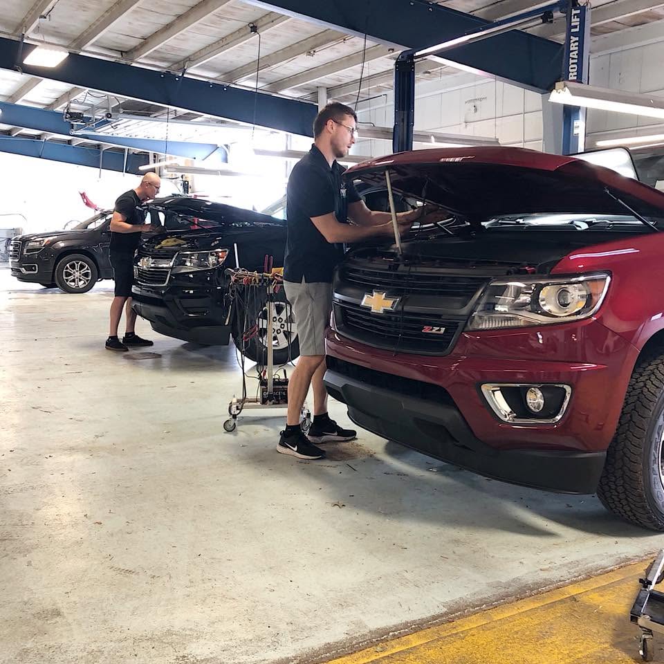 Two Dent Force technicians repairing hail-damaged vehicles in a dealership service bay