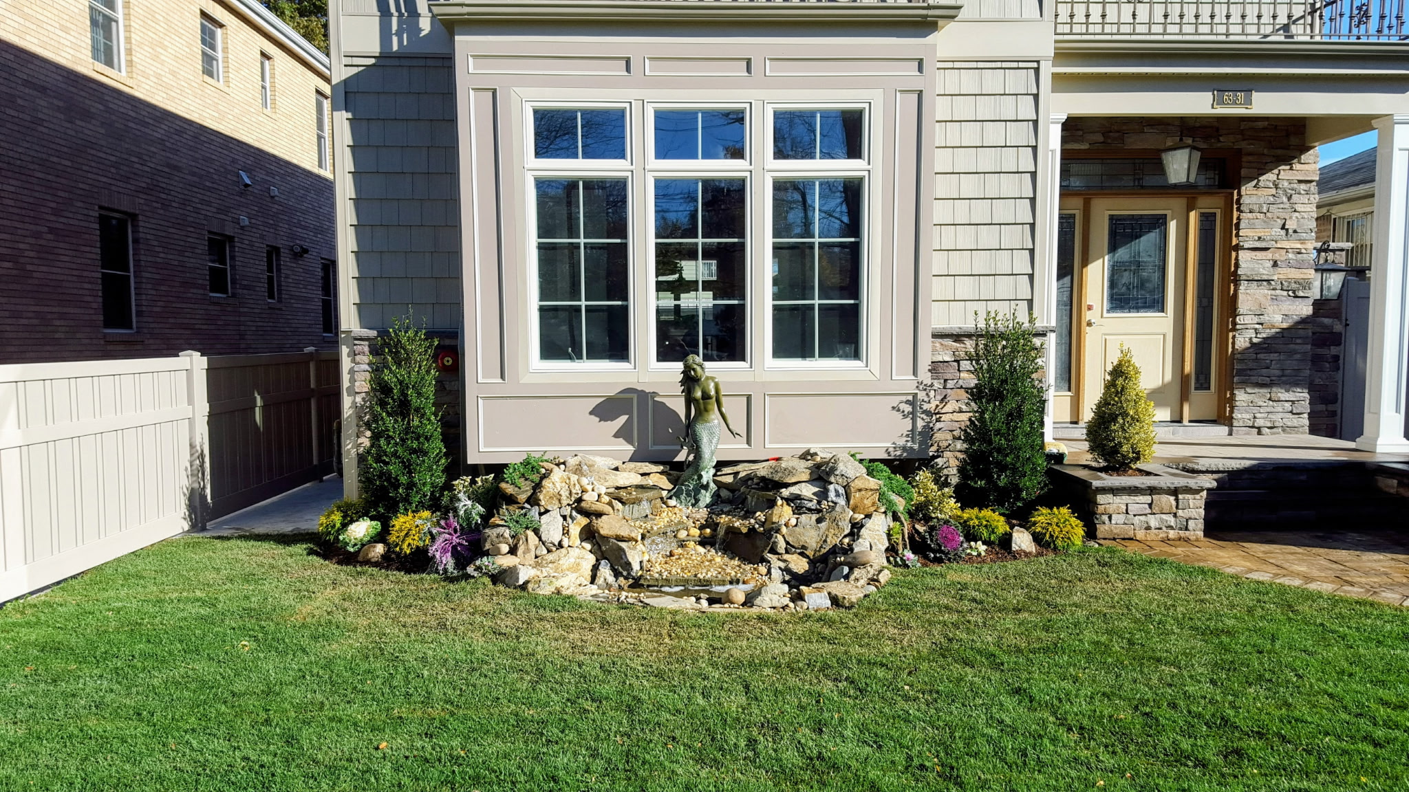 Front yard rock garden with statue centerpiece framed by evergreens under a bay window
