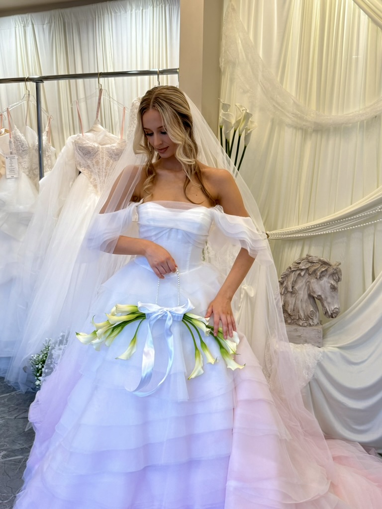 Bride in white off-shoulder ball gown with tulle skirt holding white calla lily bouquet with green ribbon