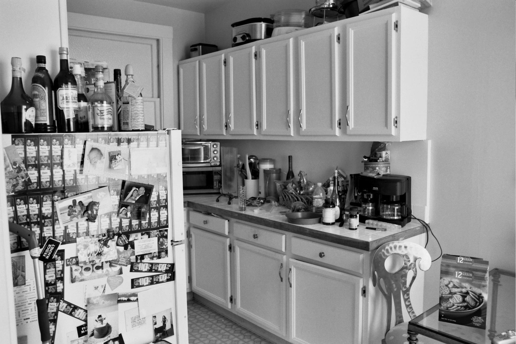 Kitchen interior covered with family photographs and mementos on refrigerator, wine bottles on white cabinetry