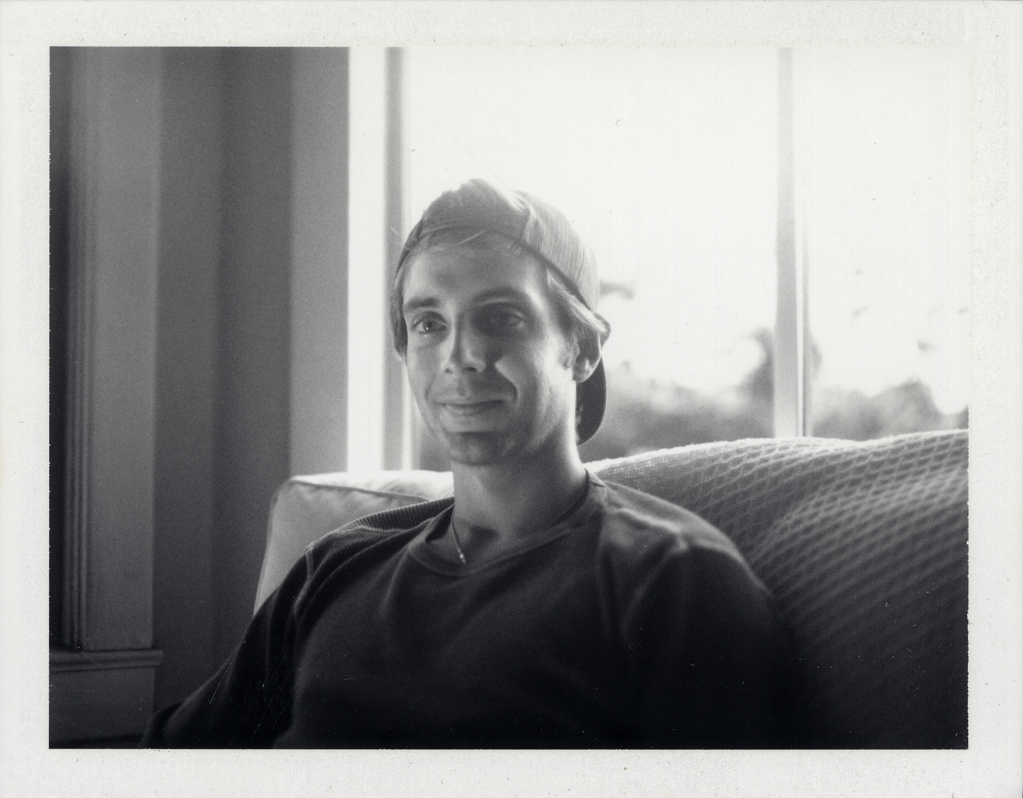Polaroid portrait of a young man in a beanie sitting on a couch by a window