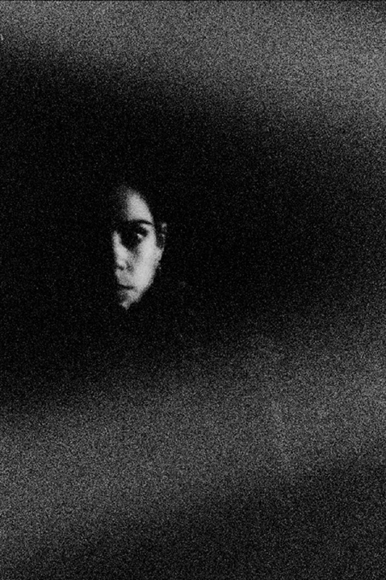 Grainy high contrast portrait of person's face emerging from darkness with atmospheric film grain texture