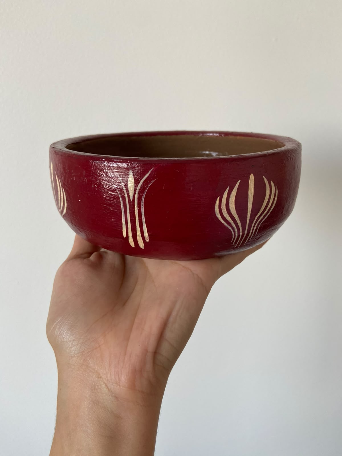 Potinho cerâmico vinho com grafismos dourados pintados à mão, segurado na mão