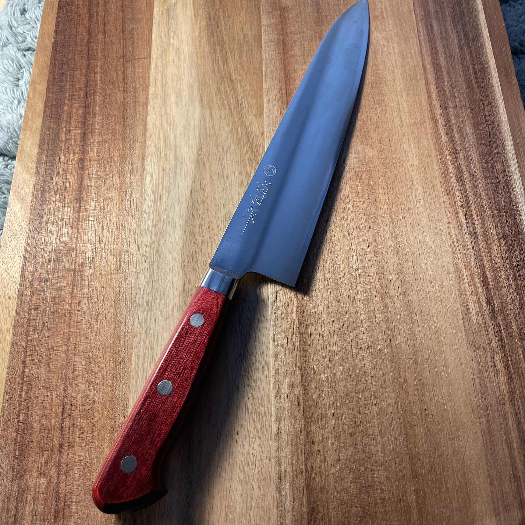 Japanese gyuto knife with reactive blue blade and red pakkawood handle on walnut cutting board