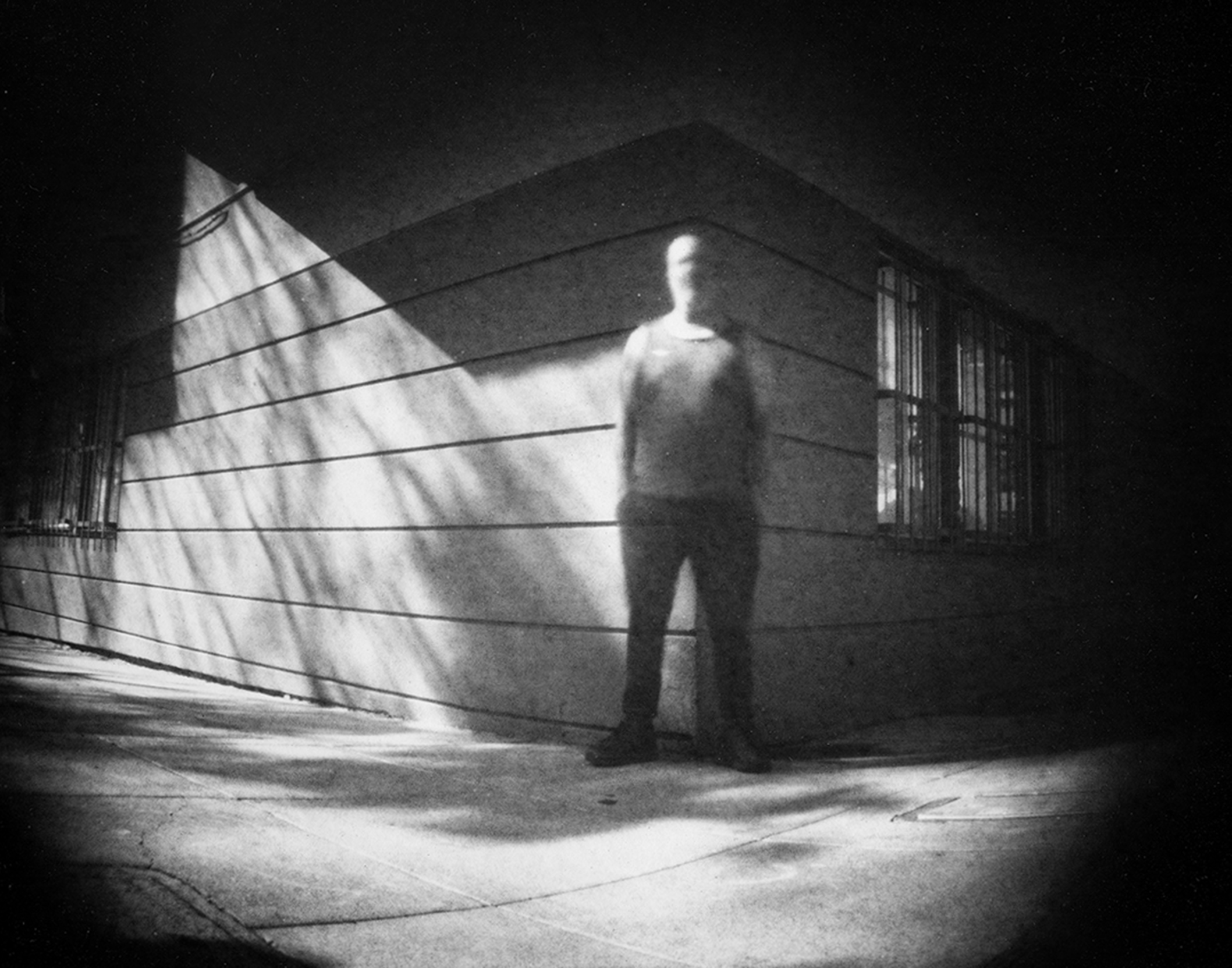 Figure standing in industrial space with dramatic light rays streaming through window creating striped patterns and ethereal atmosphere
