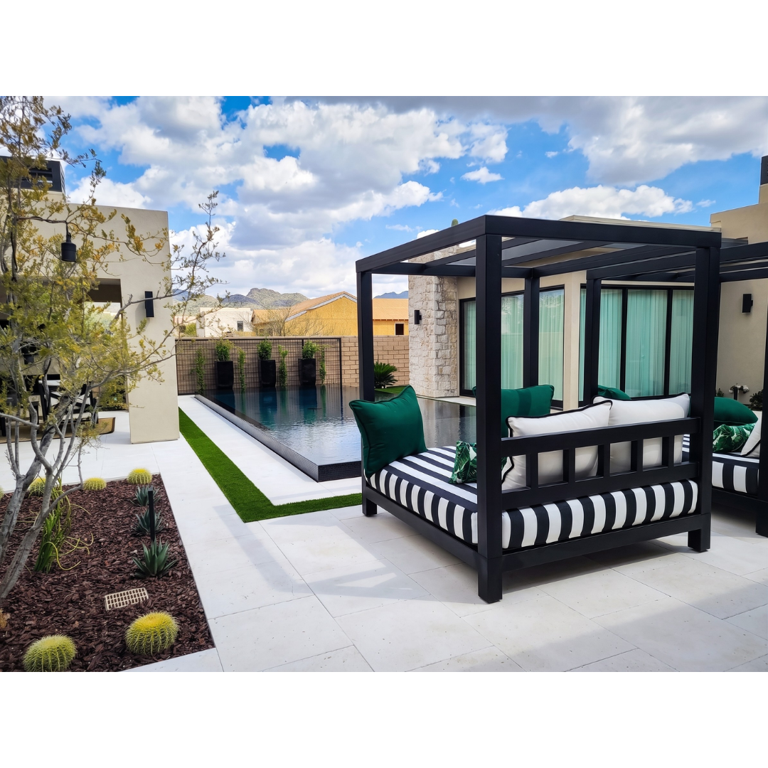 Black-framed outdoor cabana daybed with striped cushions beside an infinity pool and desert landscaping
