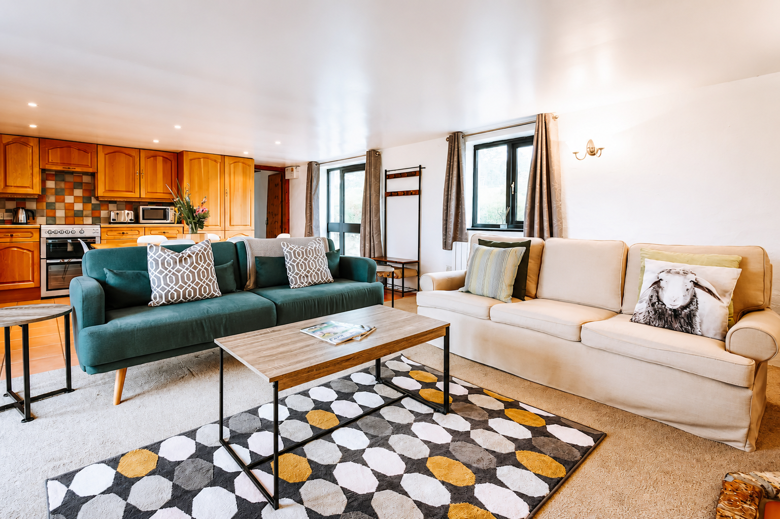 Bright open-plan living room with teal velvet sofa, cream sofa, and warm wood kitchen