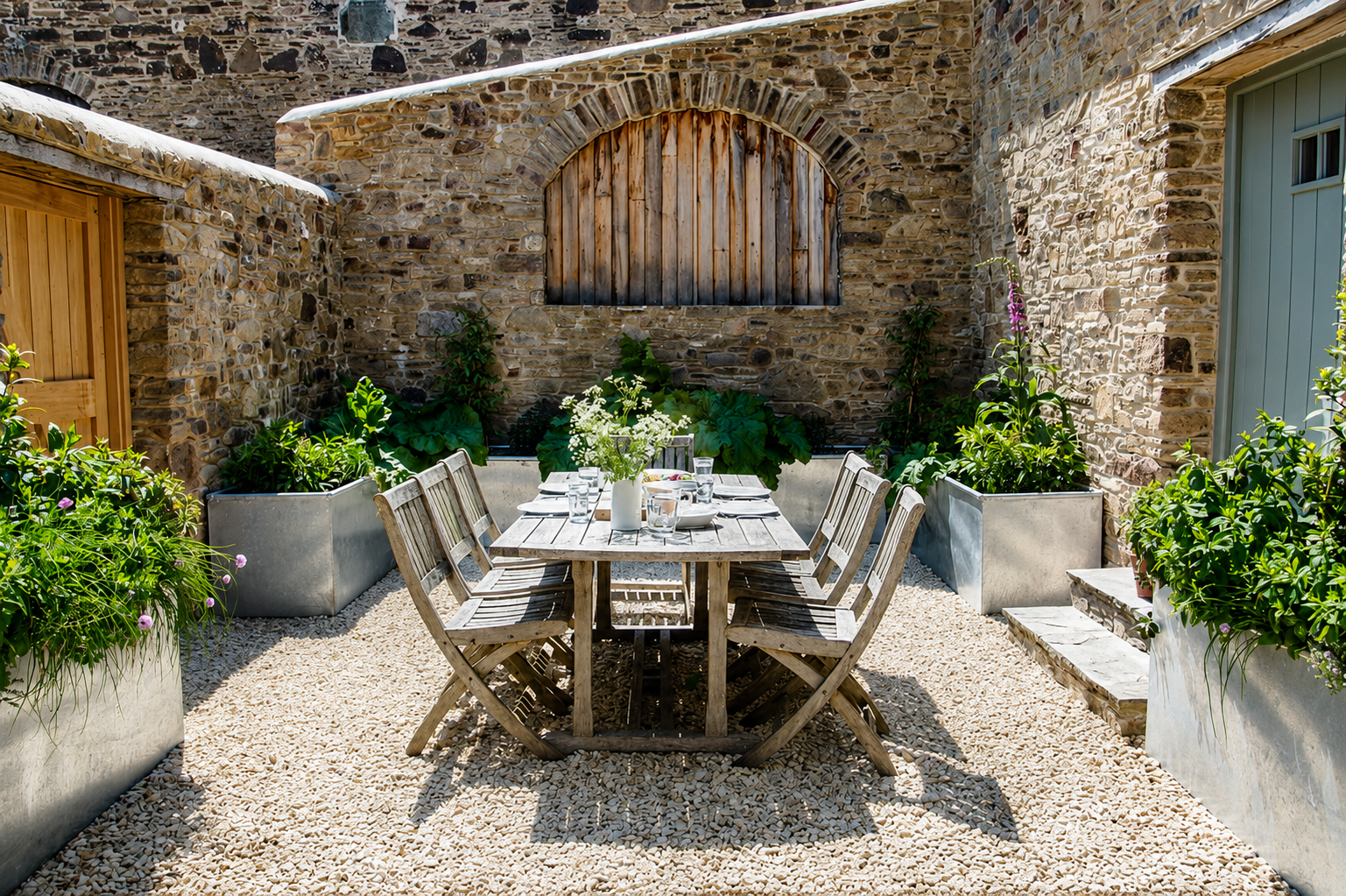 Sun-drenched courtyard with weathered teak dining table and planters in stone walls