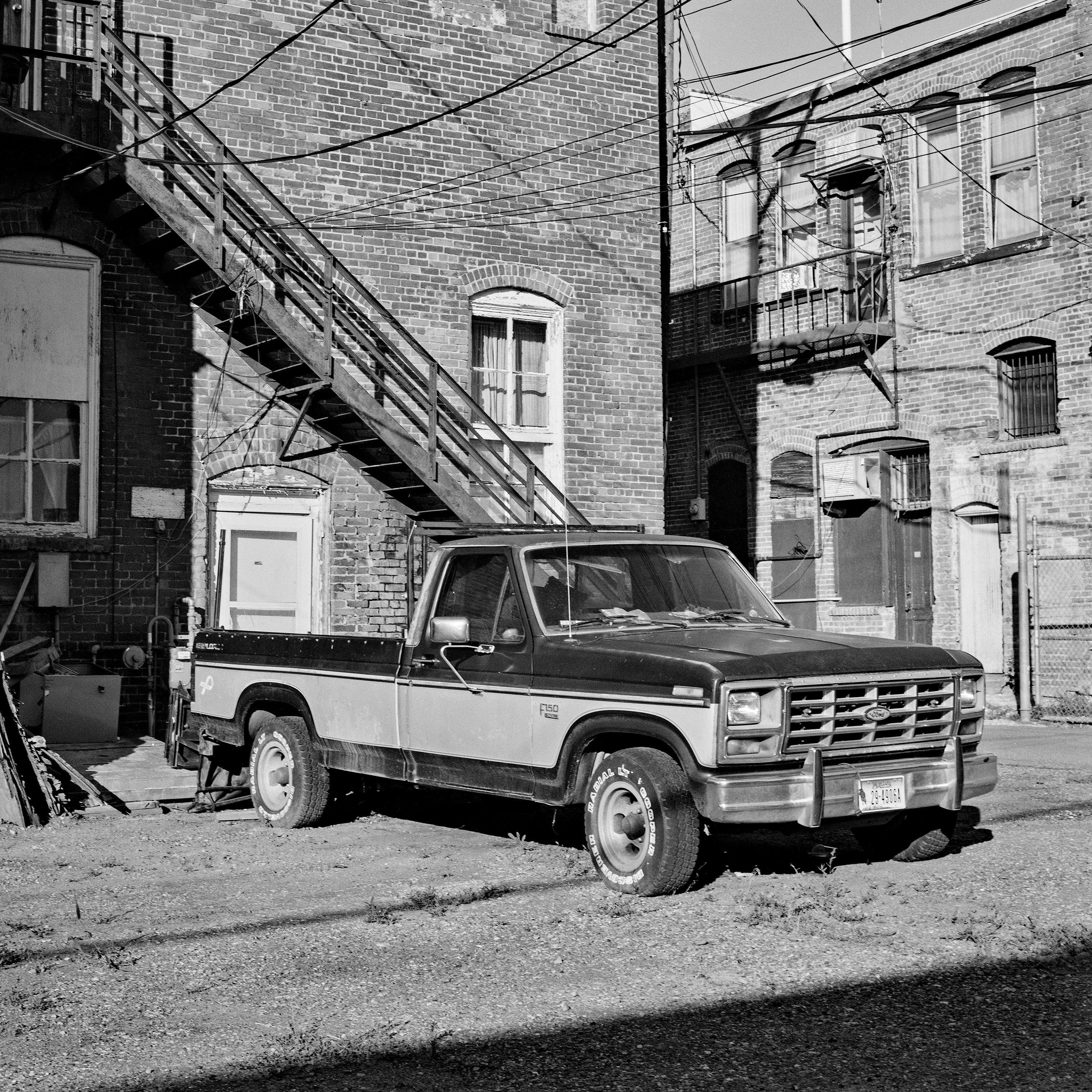 Ford F-150 pickup truck parked in brick alley with fire escapes and power lines overhead