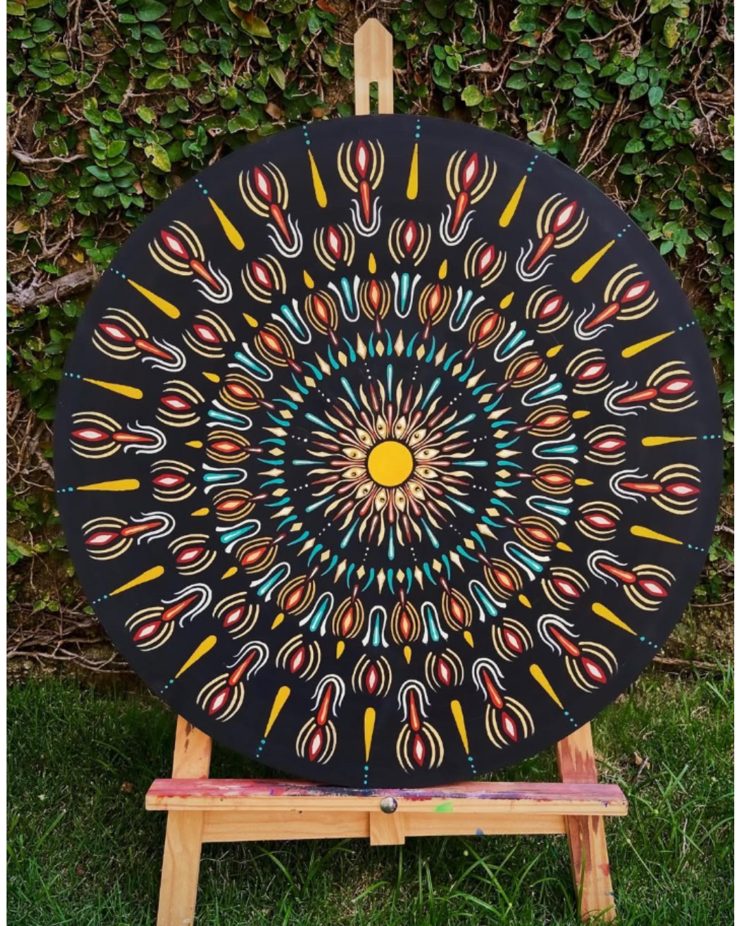 Mandala circular preta com chamas em vermelho, amarelo e turquesa no centro sobre cavalete