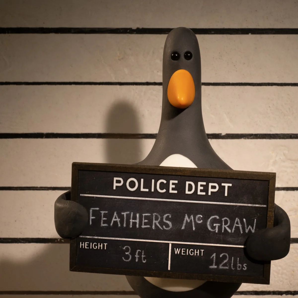 Feathers McGraw from Wallace and Gromit holding a police department mugshot board