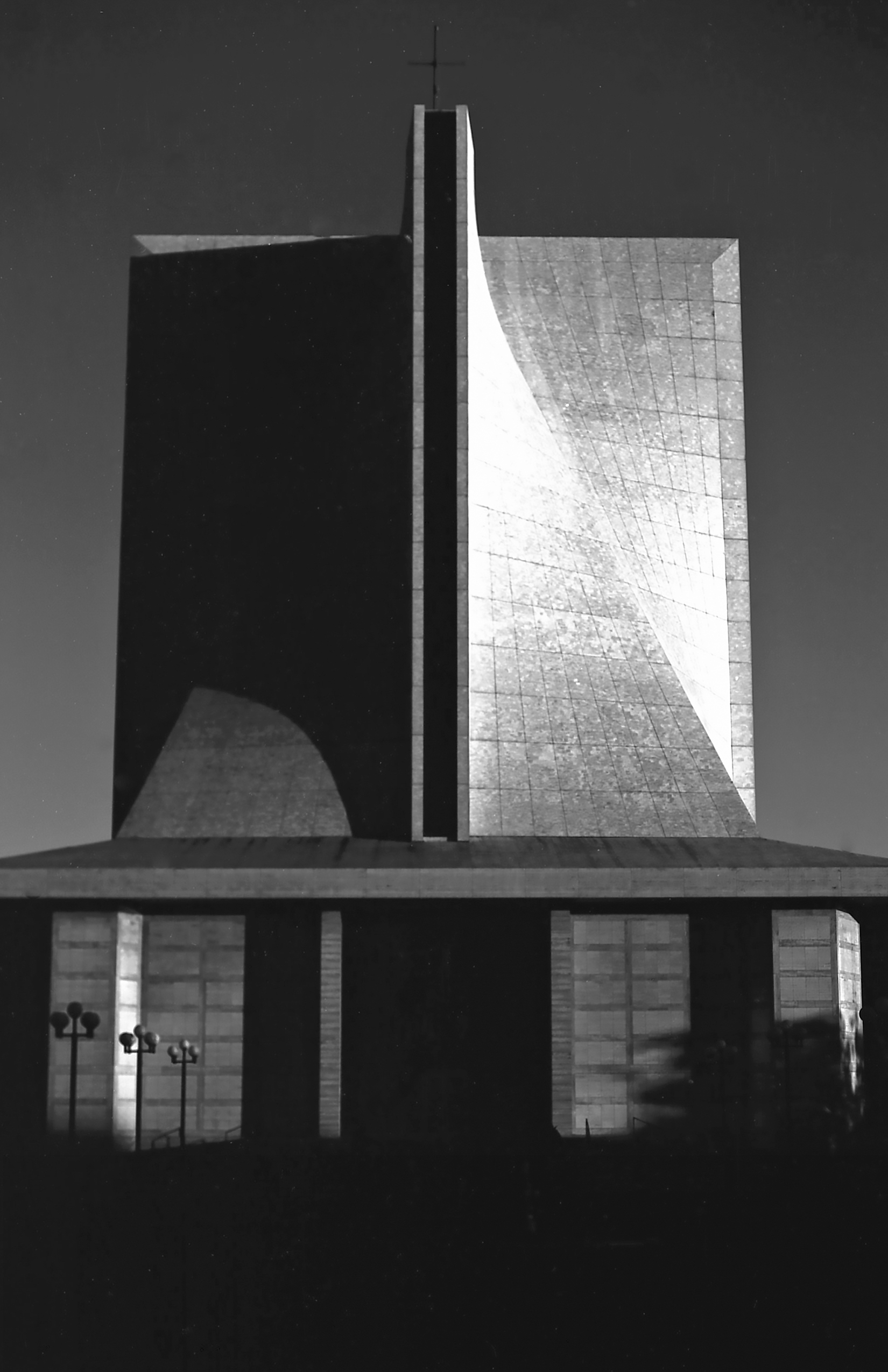Modernist building facade with geometric cross shape and angular glass surfaces creating dramatic shadows
