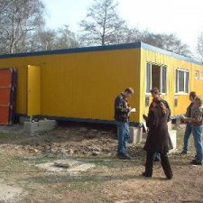 Vier Personen inspizieren den Container auf dem Gelände