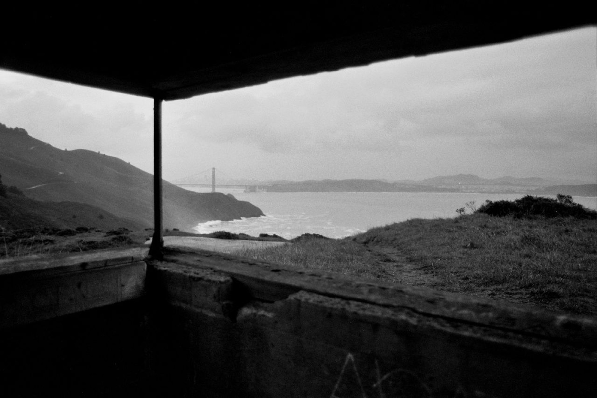 View from covered shelter looking out at San Francisco Bay with Golden Gate Bridge visible in distance hillside and vegetation