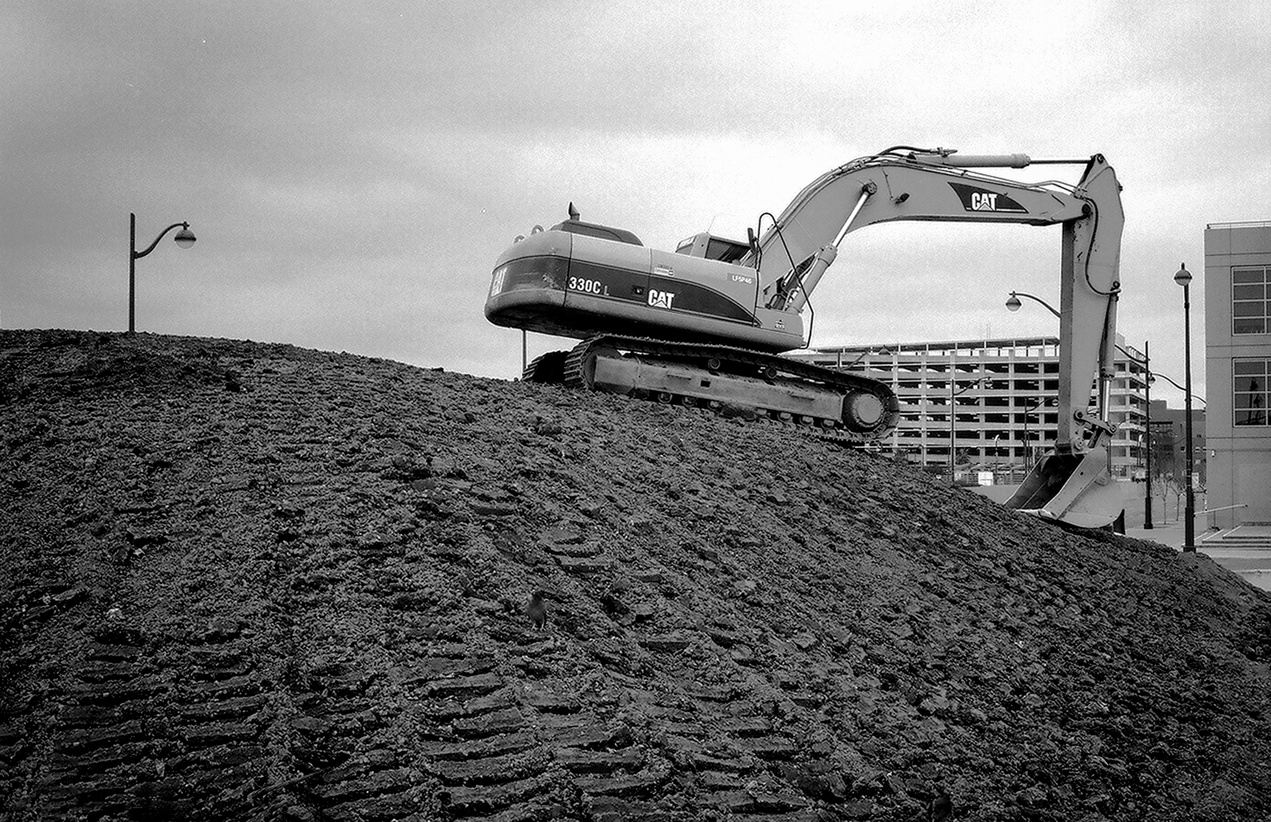 Industrial construction site with yellow CAT excavator on mound of dirt and metal infrastructure