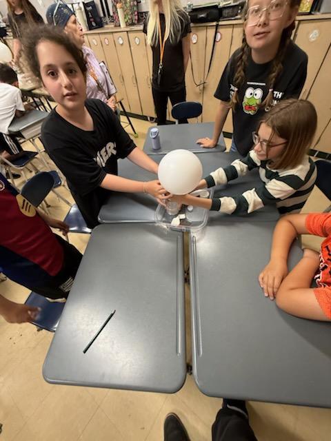 Students holding an inflated balloon over a cup during a chemistry experiment