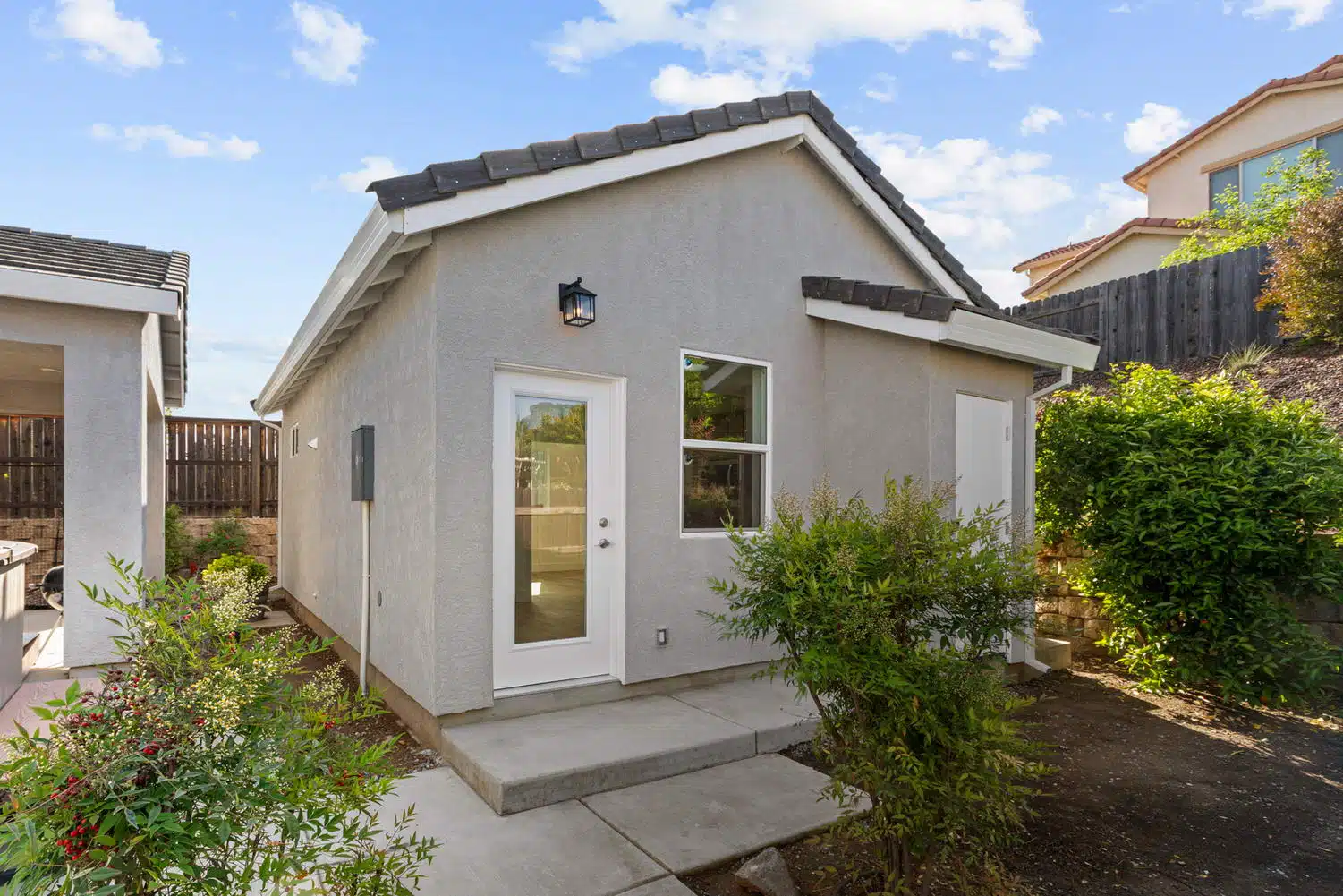Front elevation of finished stucco ADU exterior with white door and garden shrubs