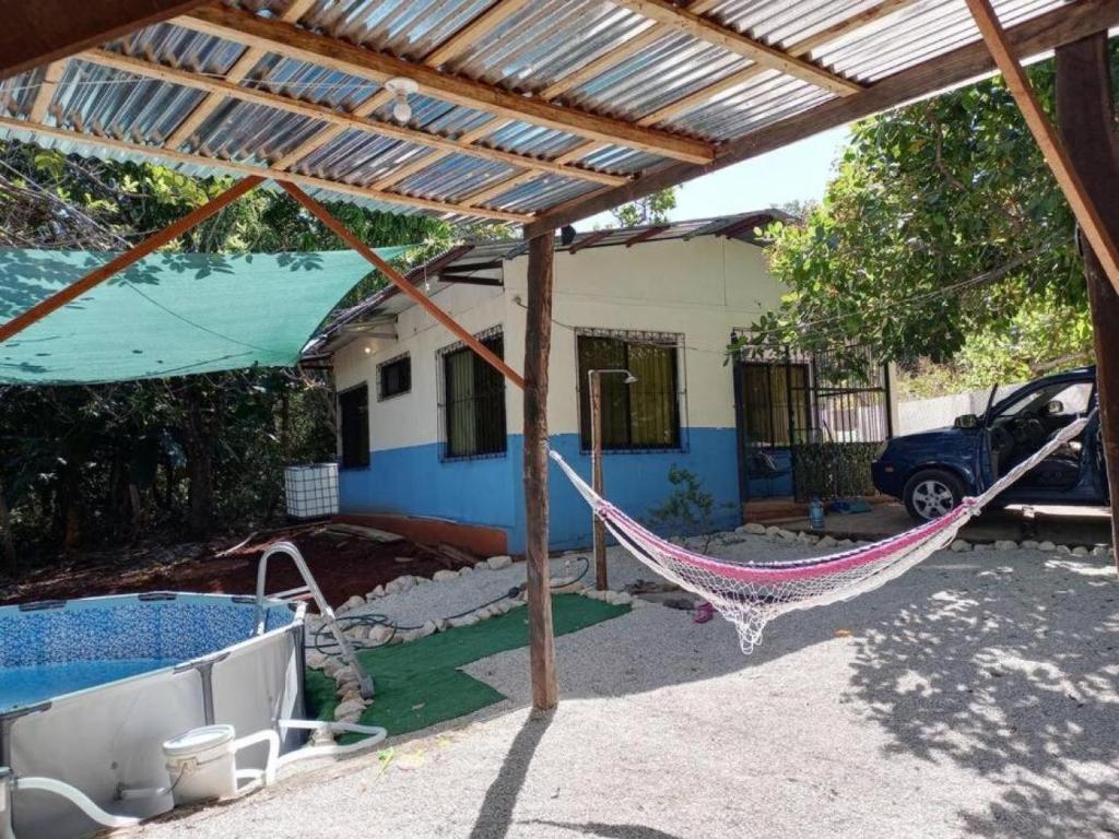 Patio cubierto con una hamaca de colores, vegetación y piscina junto a la casa