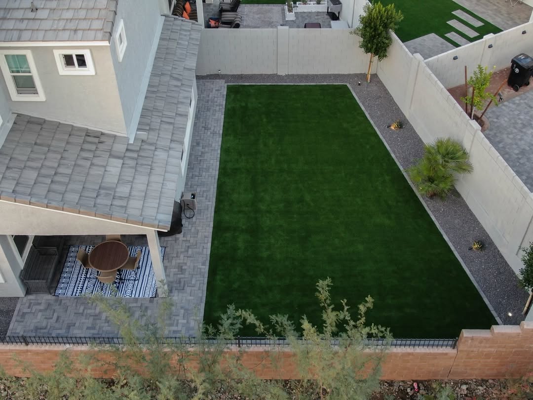 Aerial drone view of backyard with herringbone pavers, artificial turf, gravel, and palm trees