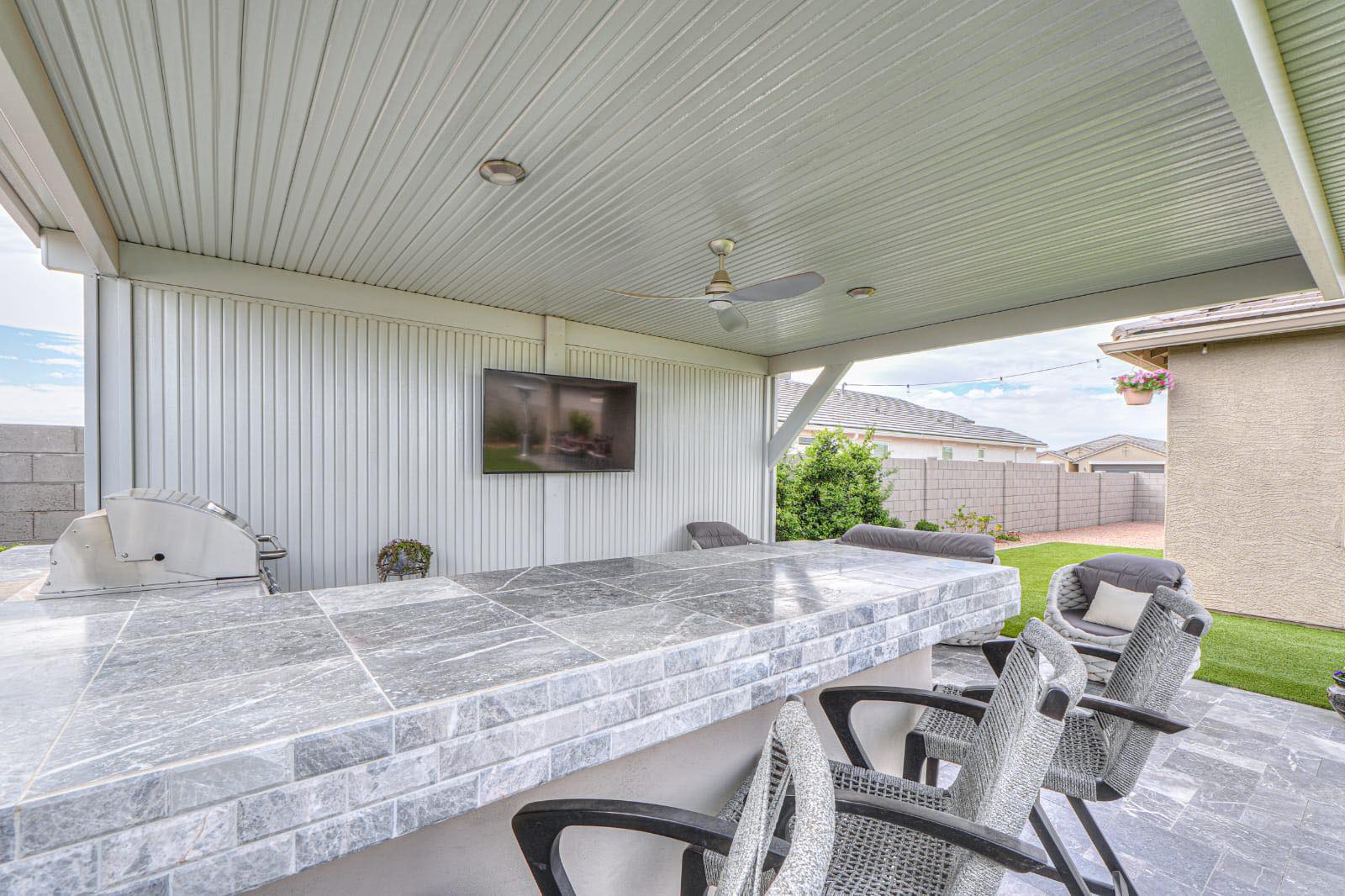 Covered patio outdoor kitchen with tile bar overlooking turf backyard