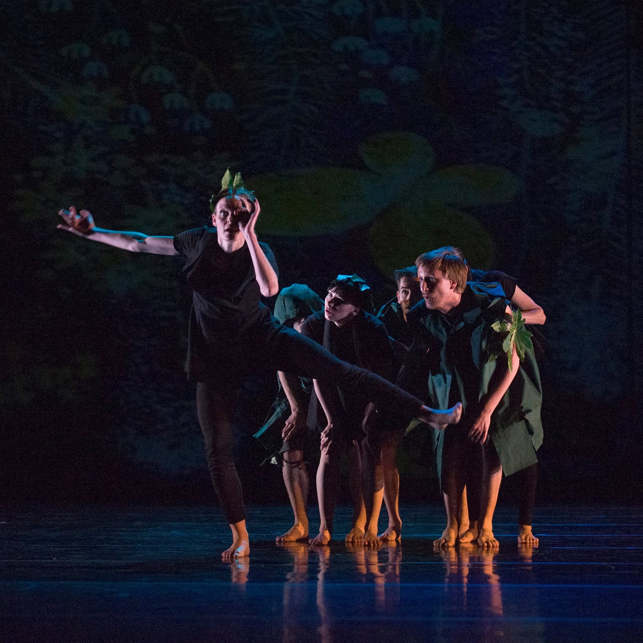 Ensemble in green and black leaf costumes on a dark stage