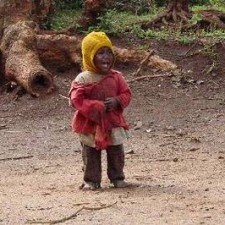 Kleines Kind mit rotem Tuch und gelbem Kopftuch lächelt auf roter Erde