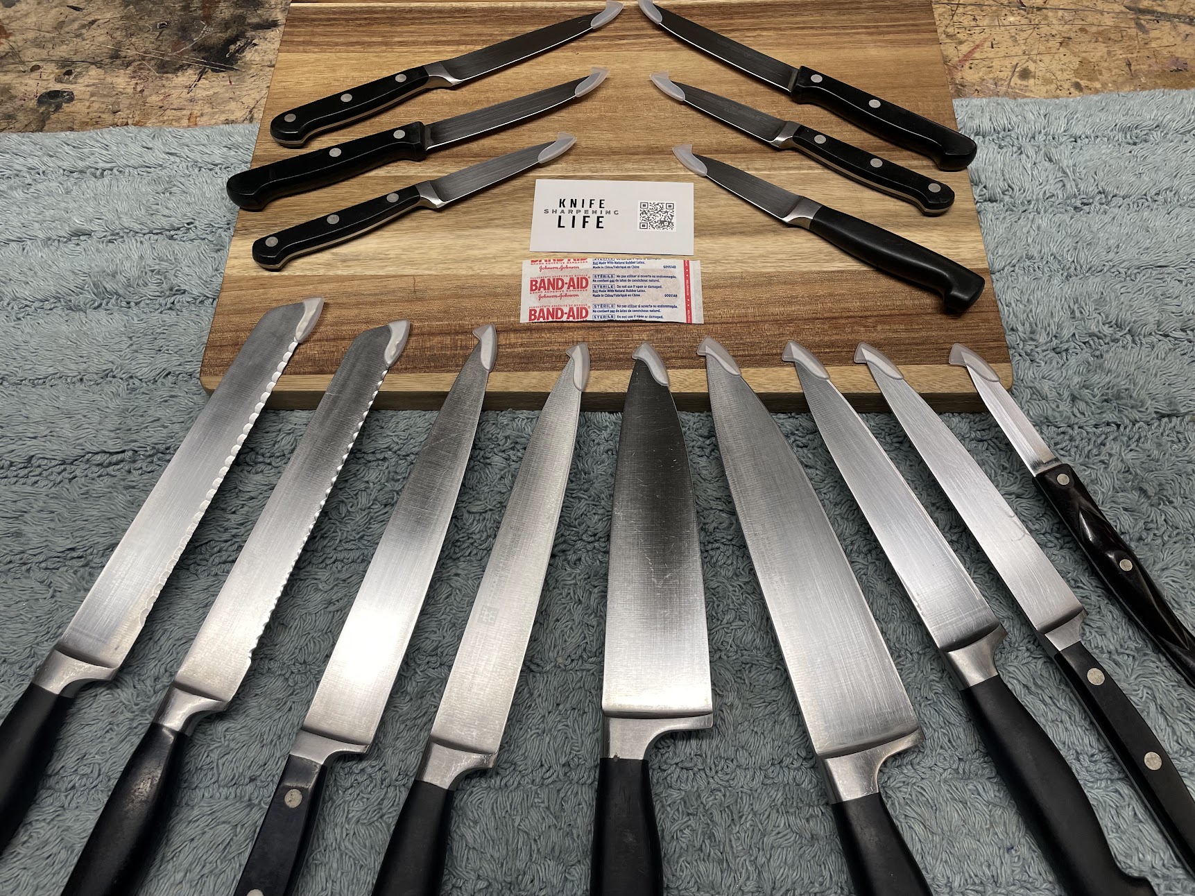 Large collection of kitchen knives arranged on cutting board with Knife Life business card