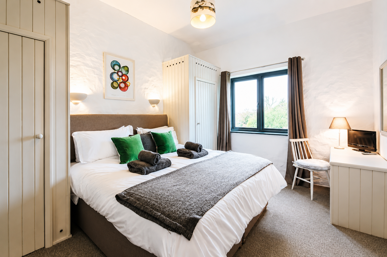Double bedroom with taupe headboard, green velvet cushions, gold lamp, and poppy-print curtains