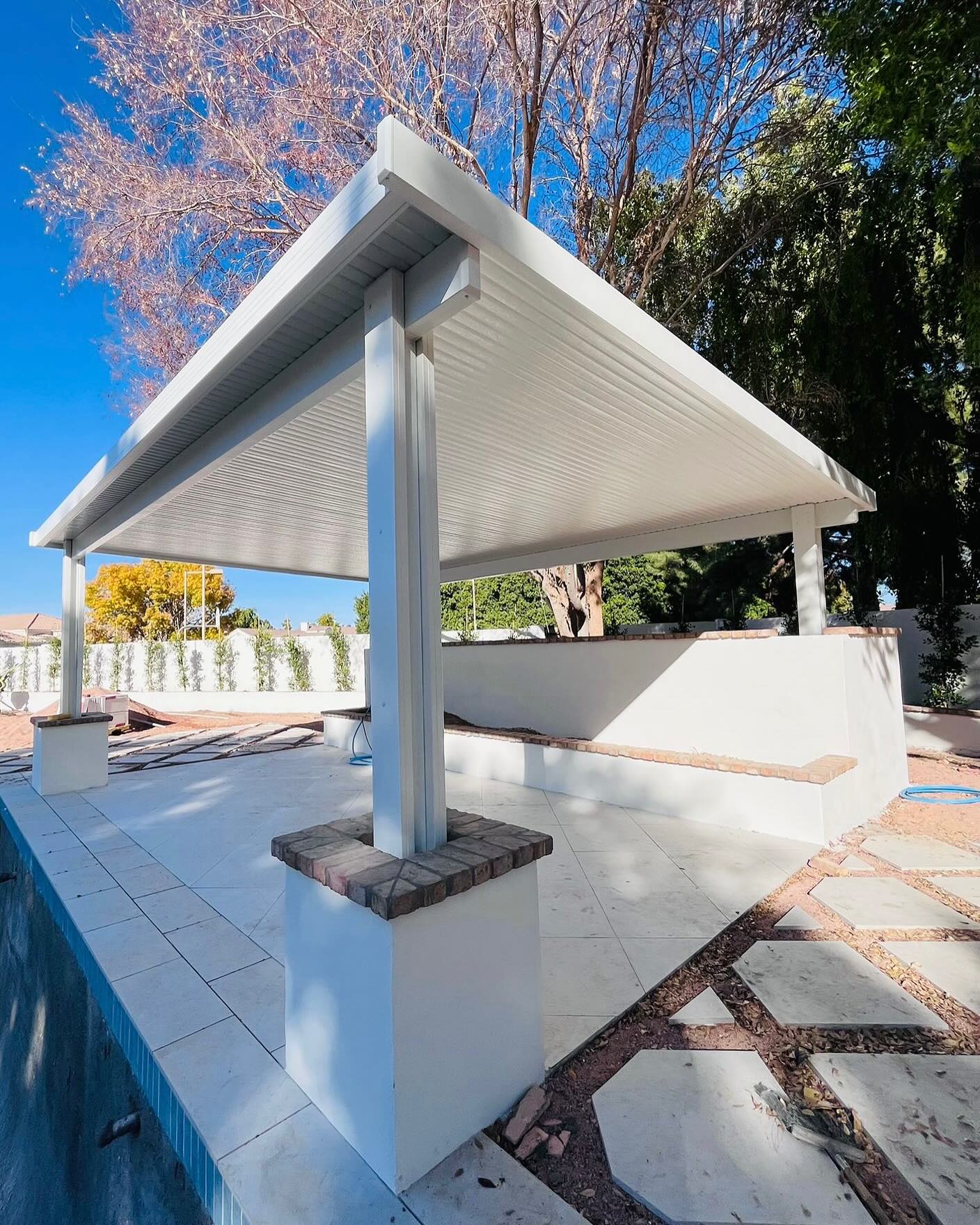 White patio cover on brick-capped columns beside a raised pool wall