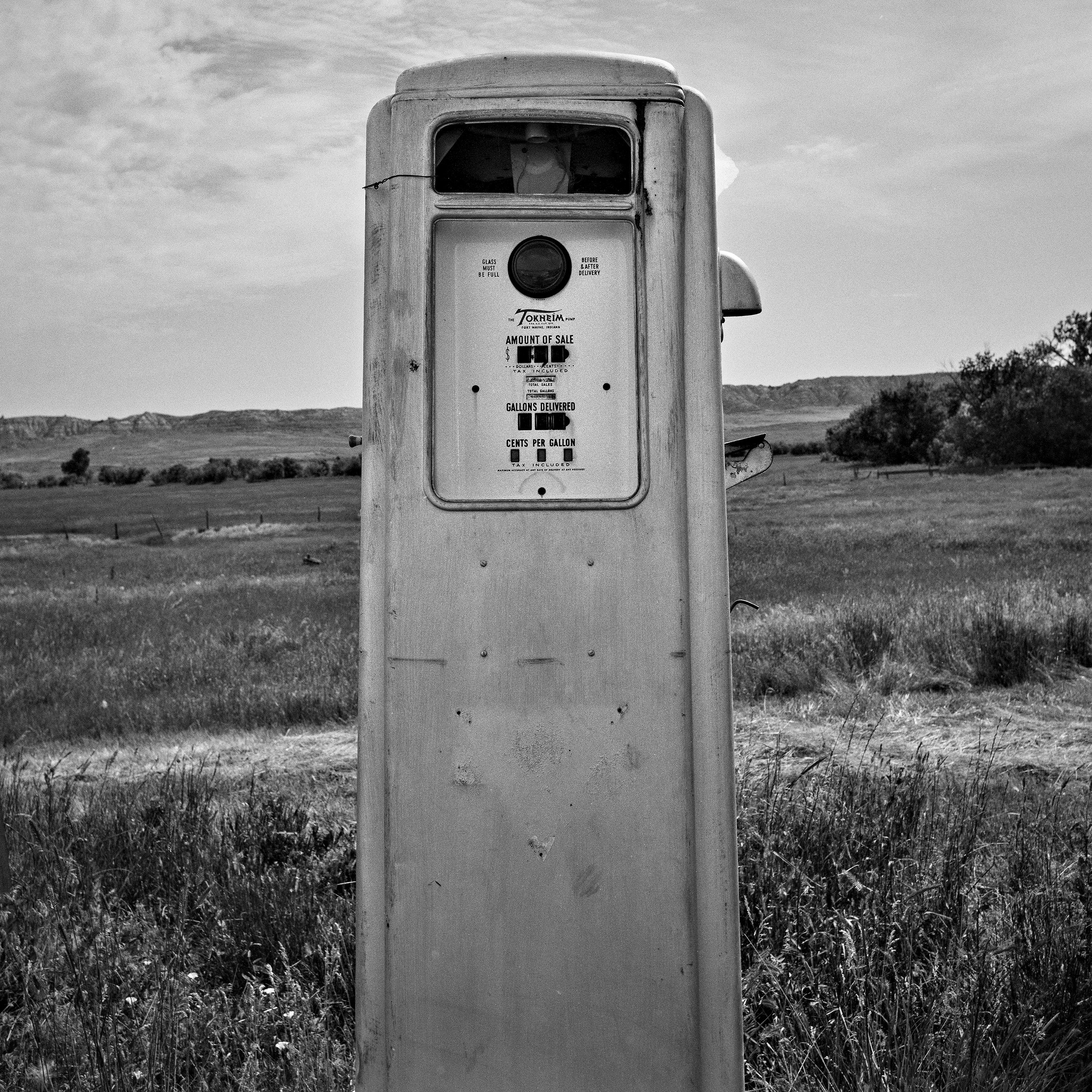 Vintage Tokheim gas pump standing alone in prairie grassland with badlands hills in distance