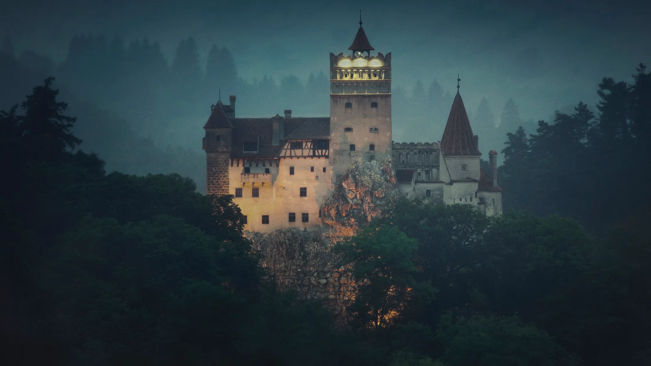 Bran Castle, known as Dracula's castle, lit up in misty Transylvanian forest at dusk