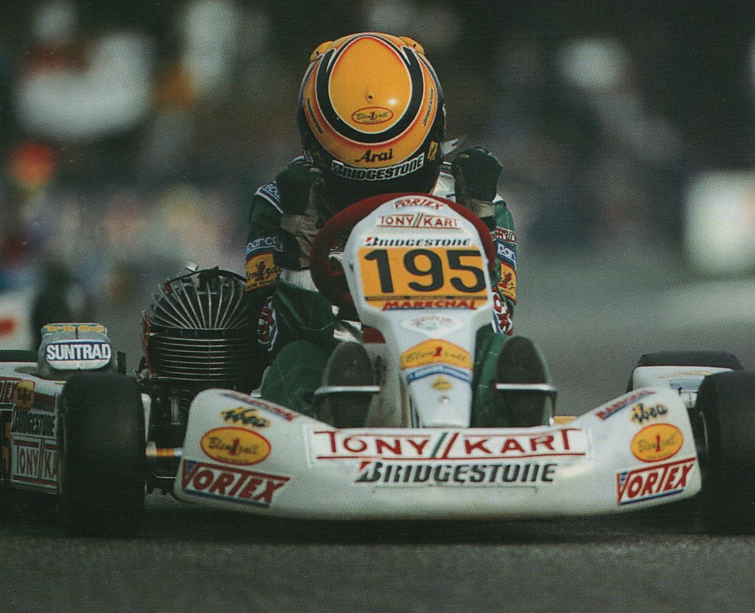 Tony Kart #195 driver in orange helmet, front-facing dramatic shot