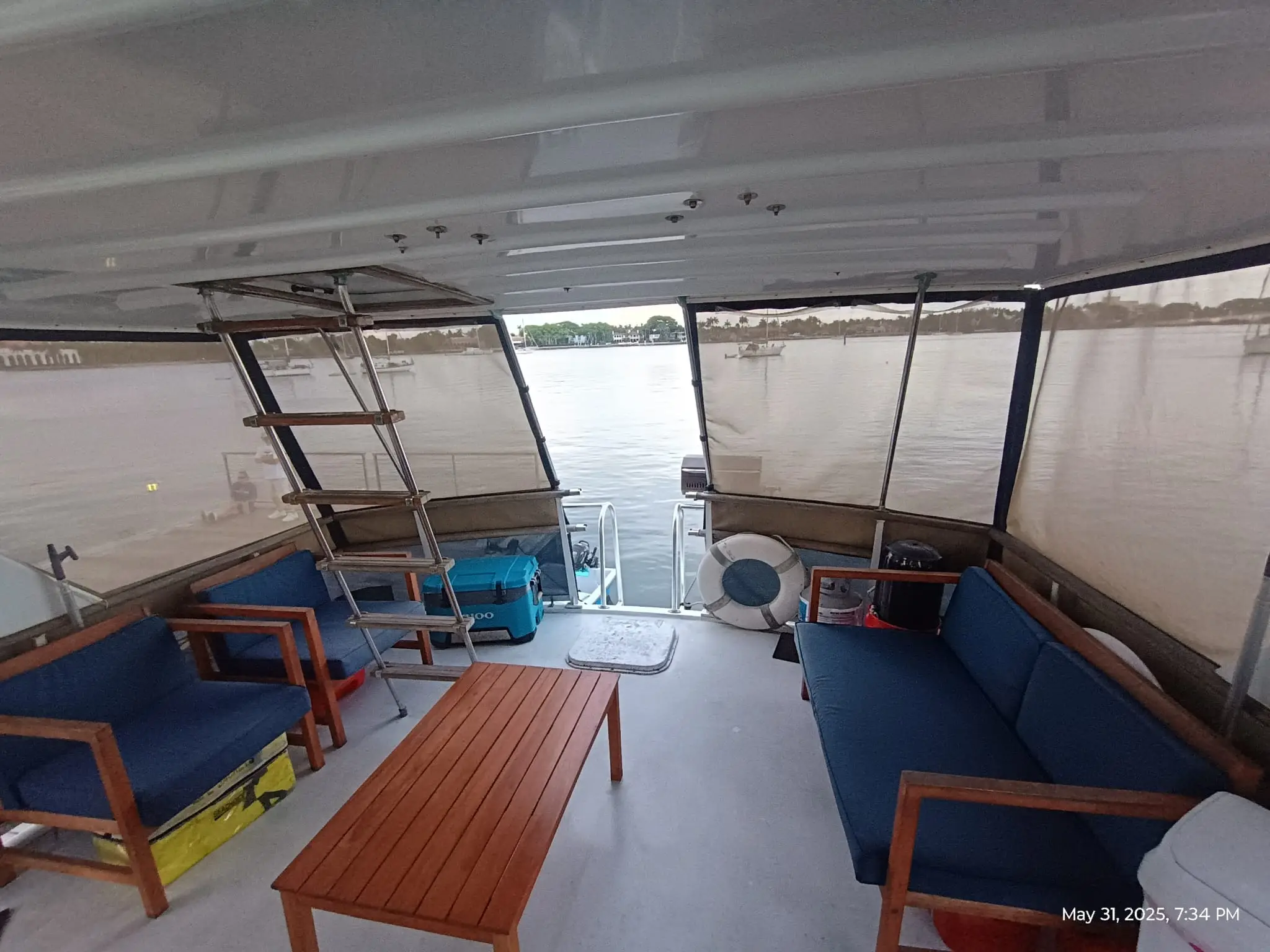 Covered aft deck lounge area of the Elite Sport Yachts 50ft Hatteras Motor Yacht showing navy blue cushioned teak-framed seating, a wooden coffee table, flybridge ladder, and open stern with water views