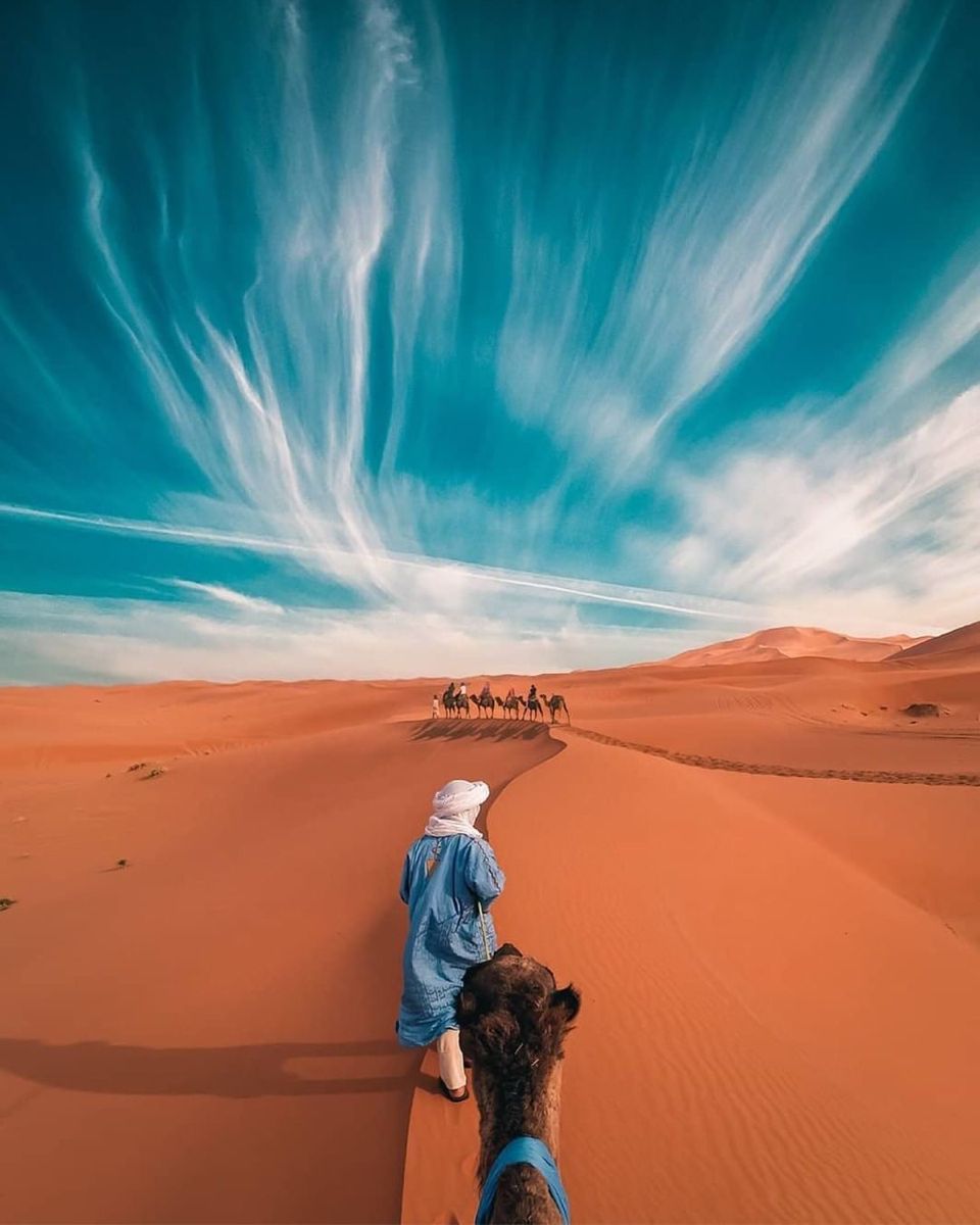 Single camel rider with another caravan visible in the distance on vast orange dunes