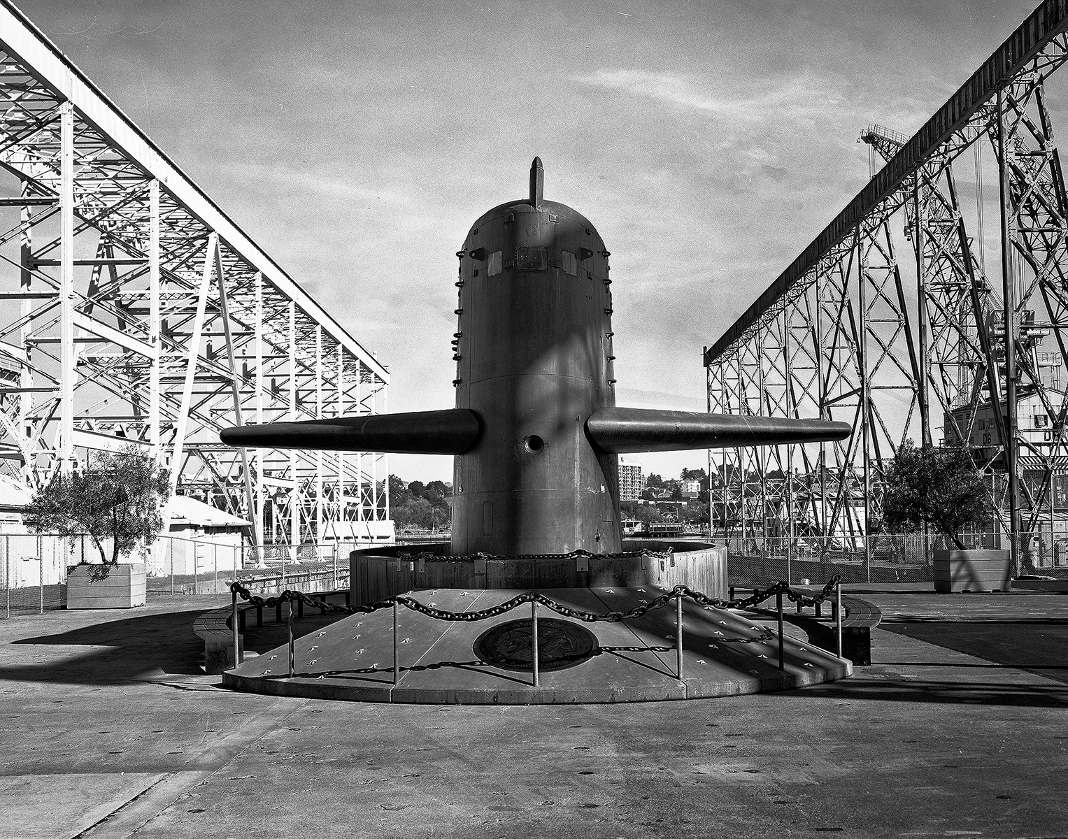 Submarine conning tower monument with extended dive planes flanked by two large steel crane structures at naval shipyard