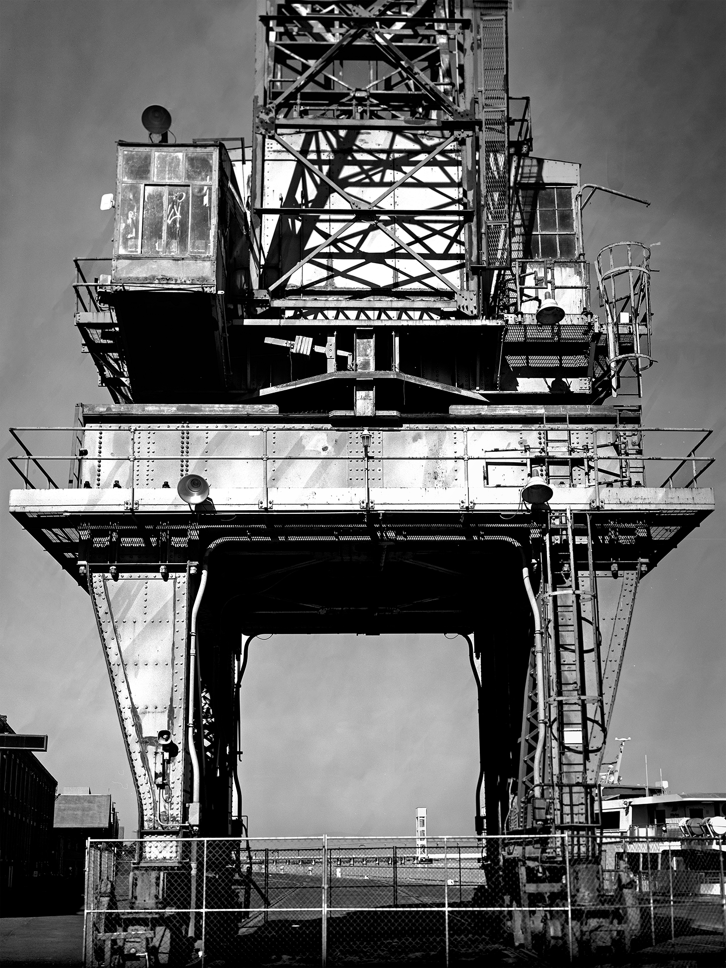 Massive industrial shipyard crane with lattice steel framework operator cabin and platforms shot from below against sky