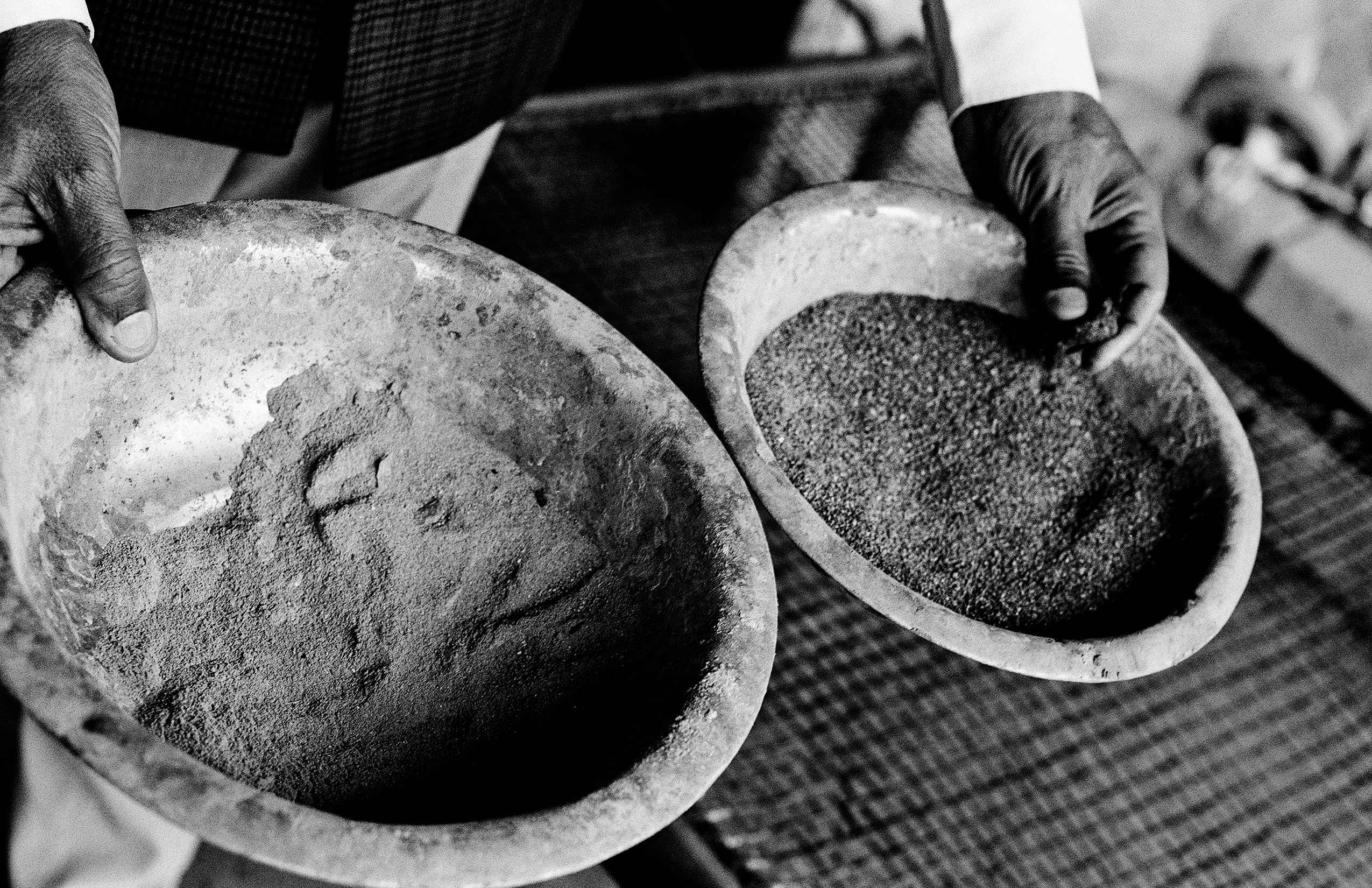 Weathered hands holding two metal bowls with spices at Indian market