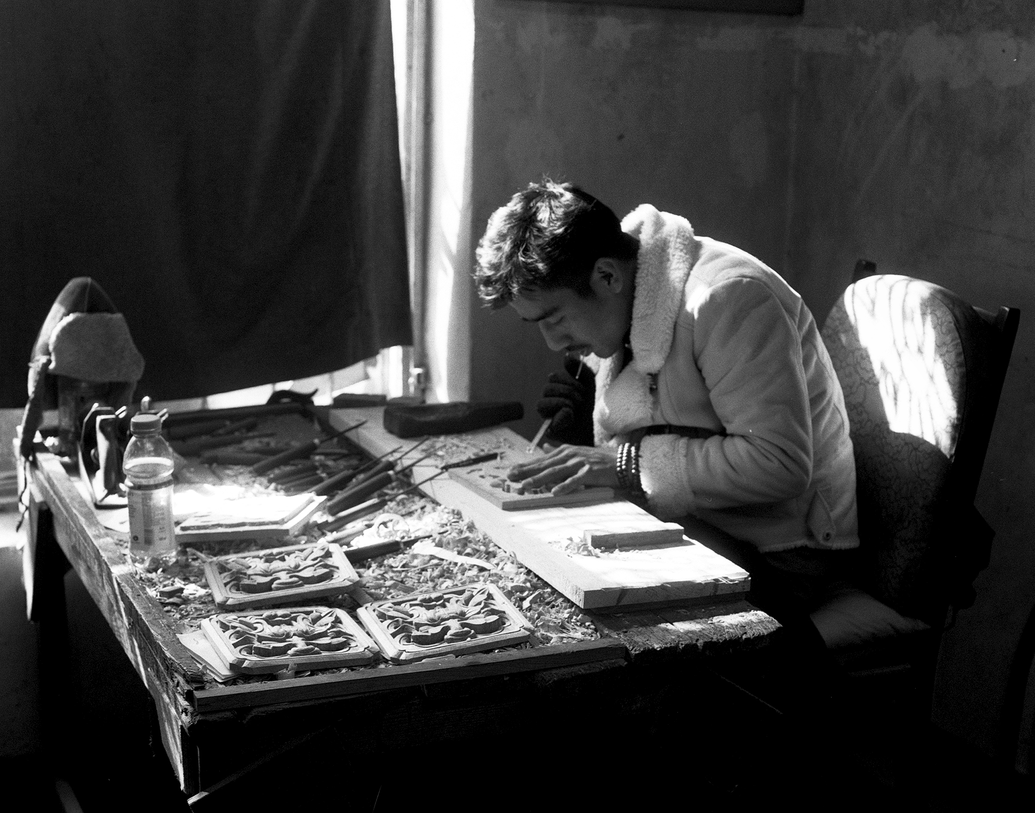 Artisan carving intricate wooden panels in workshop with natural window light