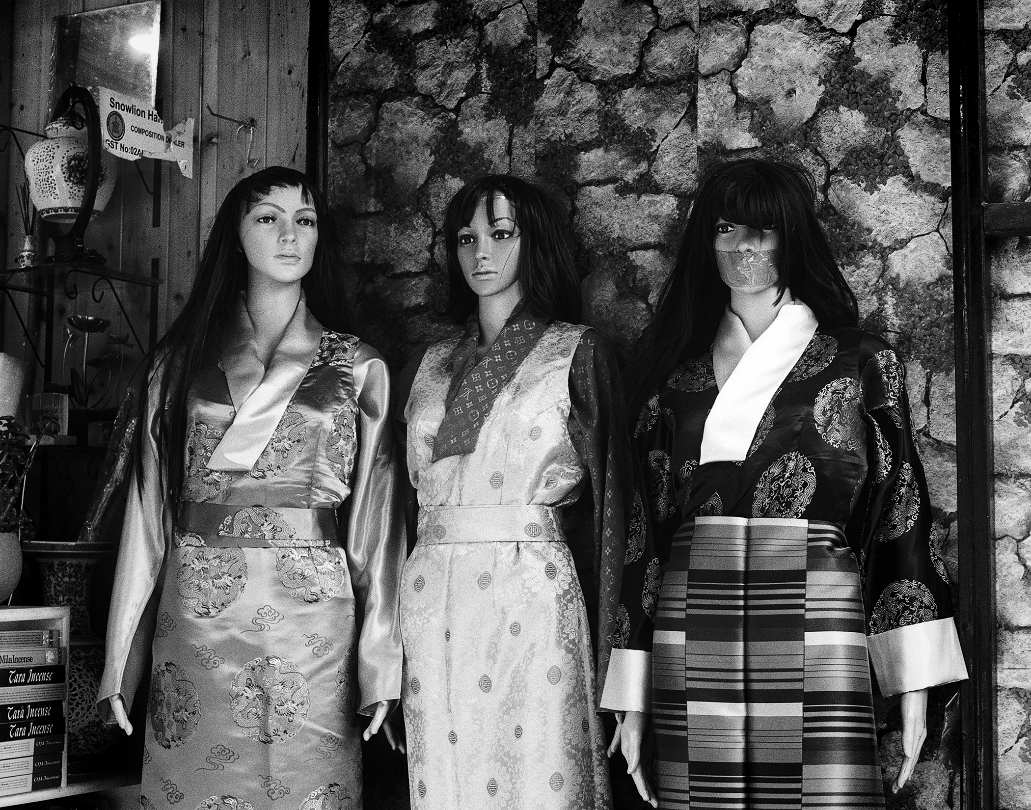 Three mannequins wearing traditional silk garments against stone wall