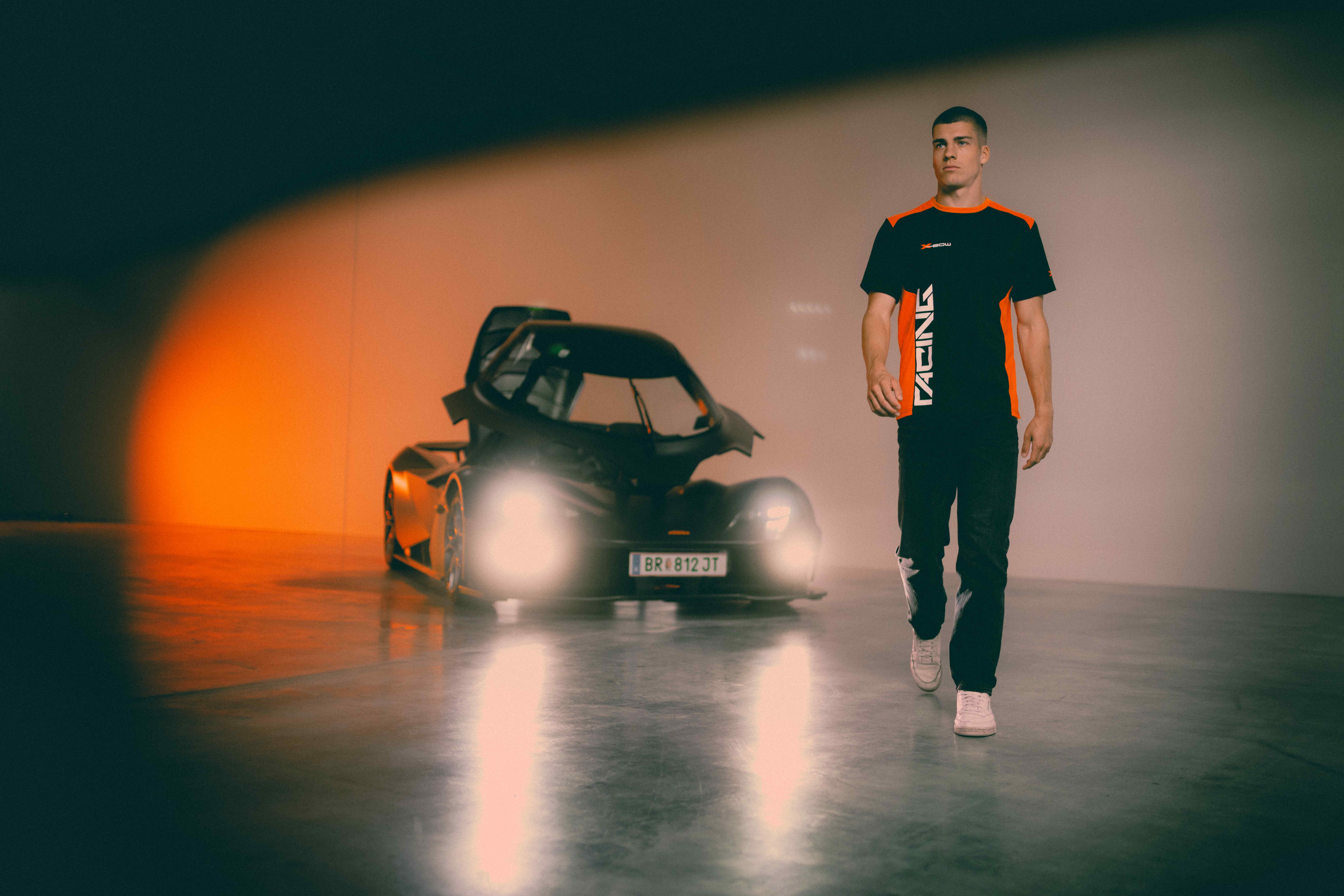 Man in KTM X-BOW racing apparel walking through a showroom beside a black KTM X-BOW